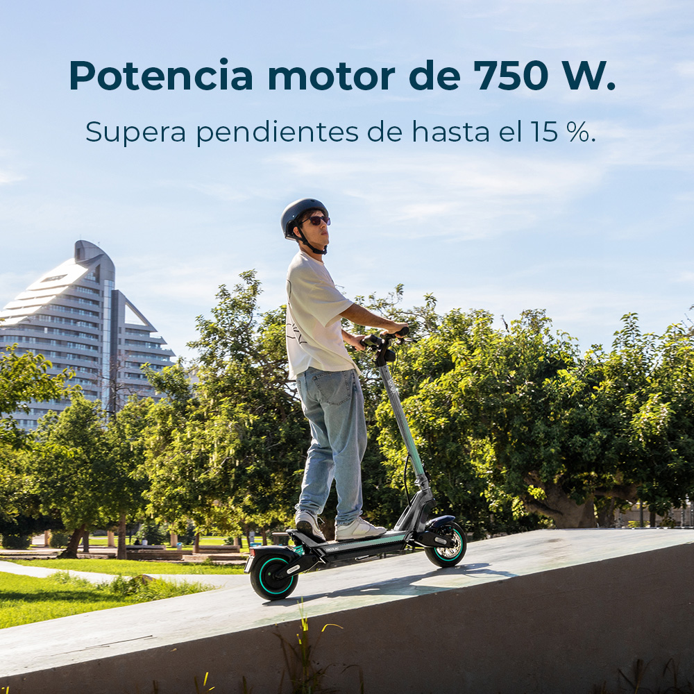 Un hombre monta en un patinete eléctrico sobre una rampa. Lleva casco y gafas de sol. Hay árboles y edificios al fondo.