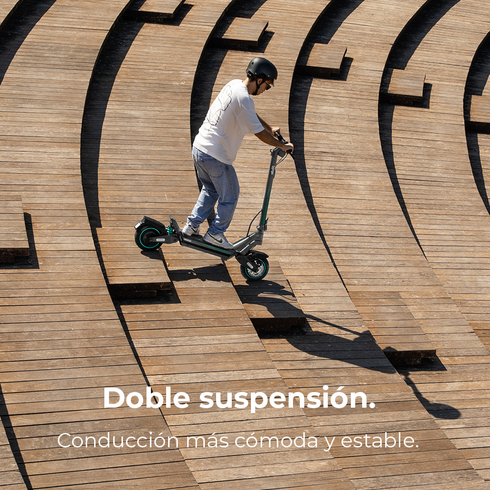 Un hombre monta en un patinete eléctrico por una rampa de madera. Lleva casco, vaqueros y una camisa blanca. El patinete es negro y verde.