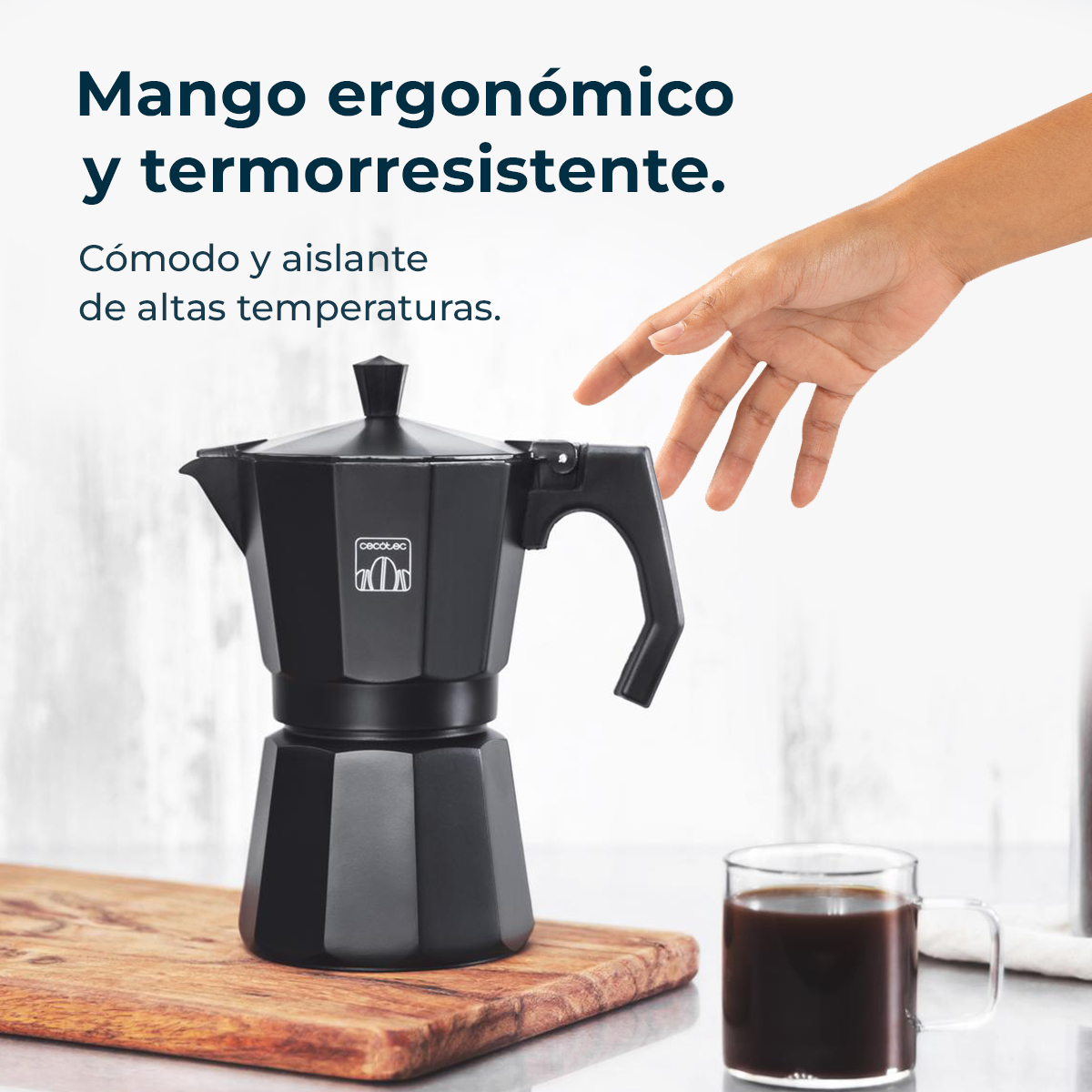 Czarny ekspres do kawy na drewnianej desce. Ręka sięga w jego stronę. Szklanka kawy jest w prawym dolnym rogu.