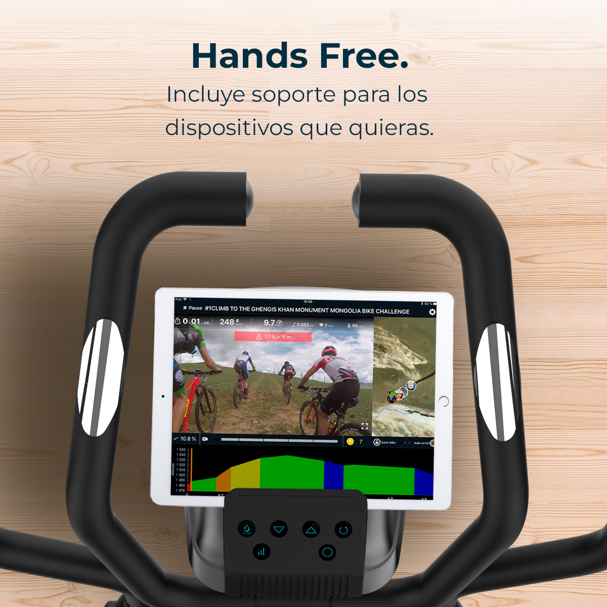 Una bicicleta estática con una tableta que muestra un desafío de ciclismo. Manijas negras y un panel de control en primer plano. Fondo de madera.