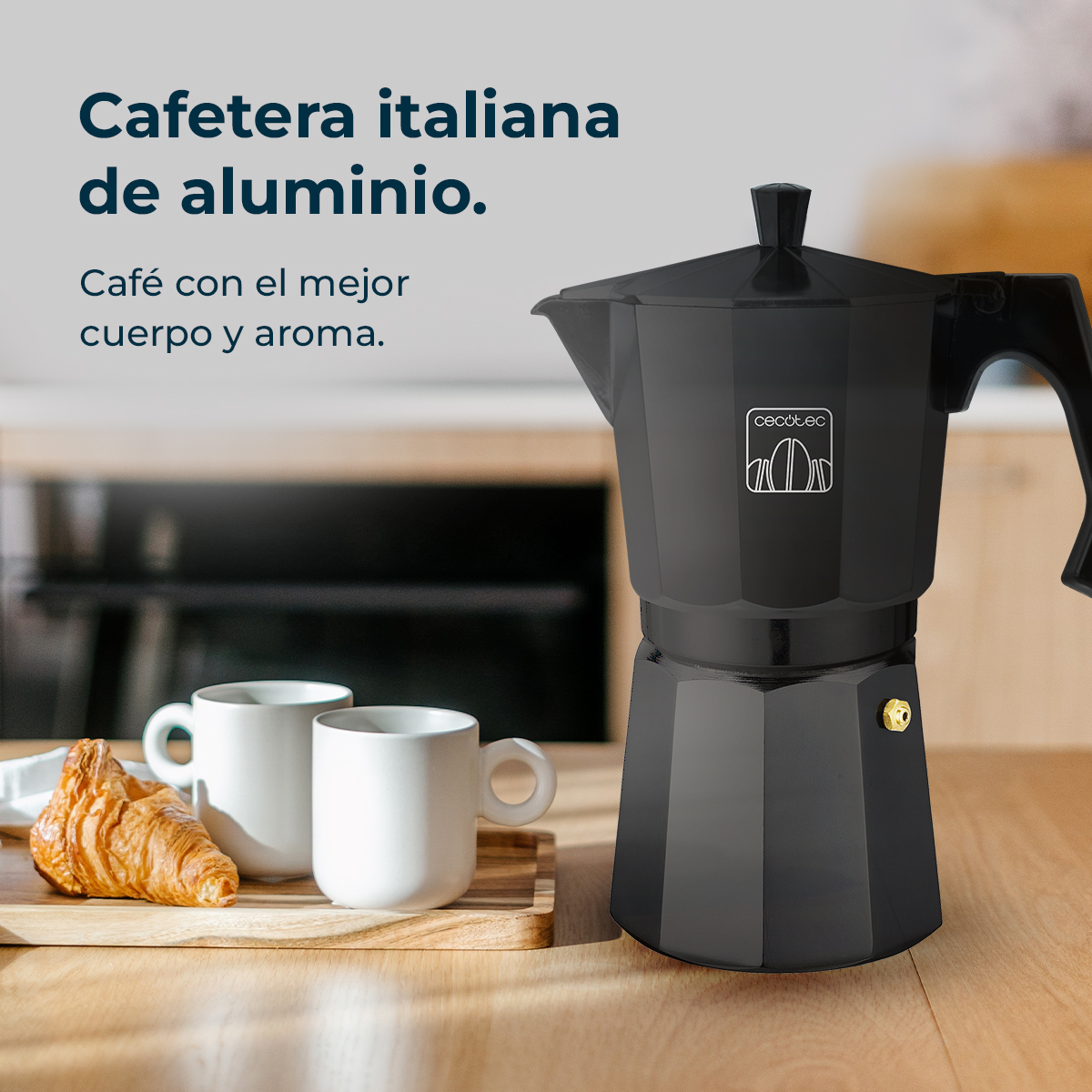 Cafetera italiana negra sobre una mesa de madera. Dos tazas blancas y un cruasán sobre una tabla de madera.