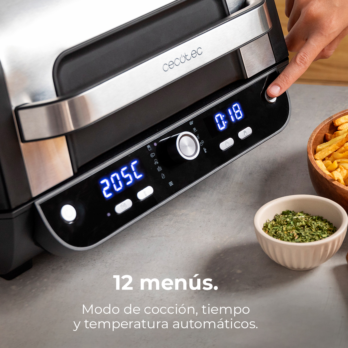 Ręka naciska przycisk na grillu. Wyświetlacz pokazuje 205C, 0:18. W pobliżu frytki i zioła w miskach.