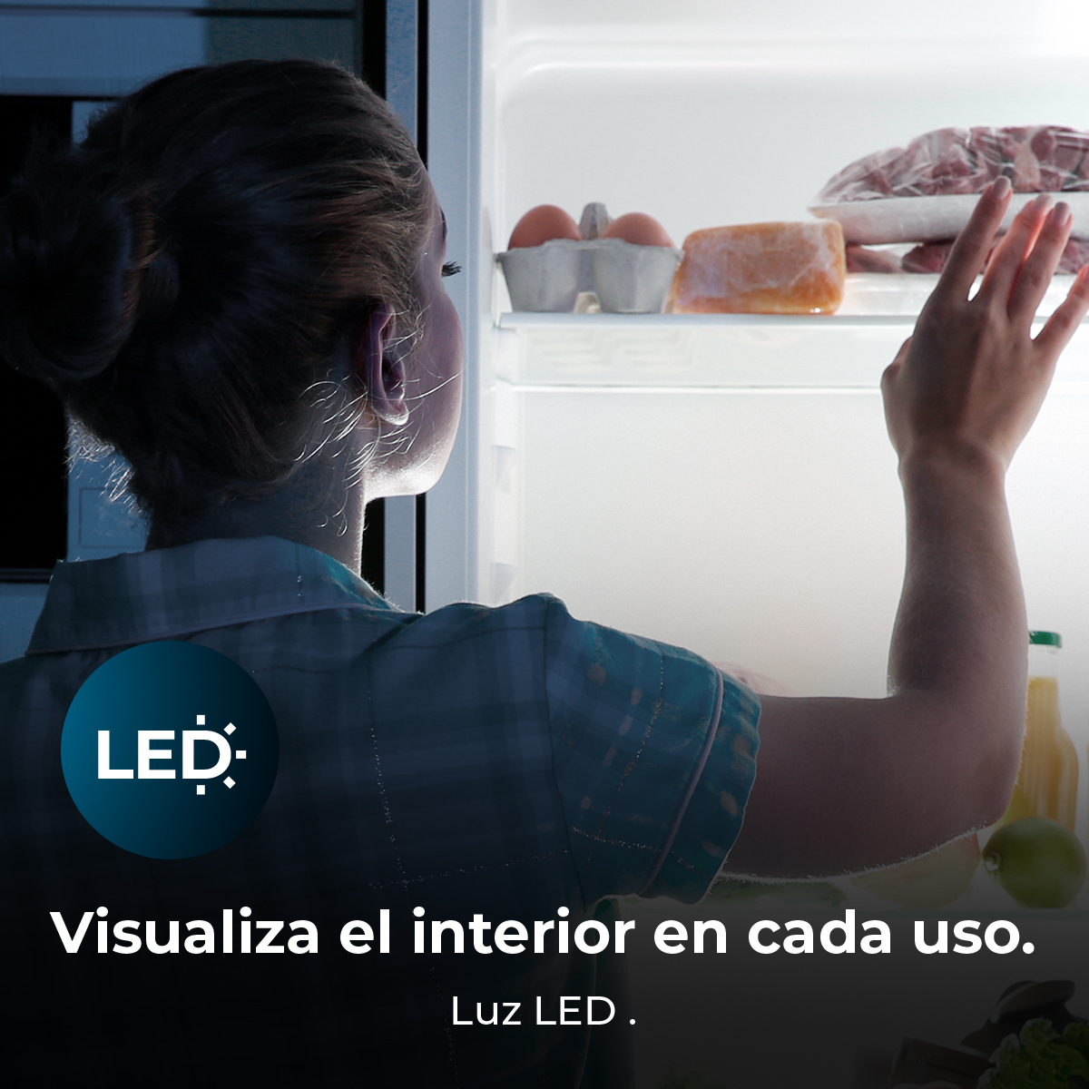 Una mujer alcanza un refrigerador iluminado por LED. Huevos, queso y carne envasada son visibles en un estante.
