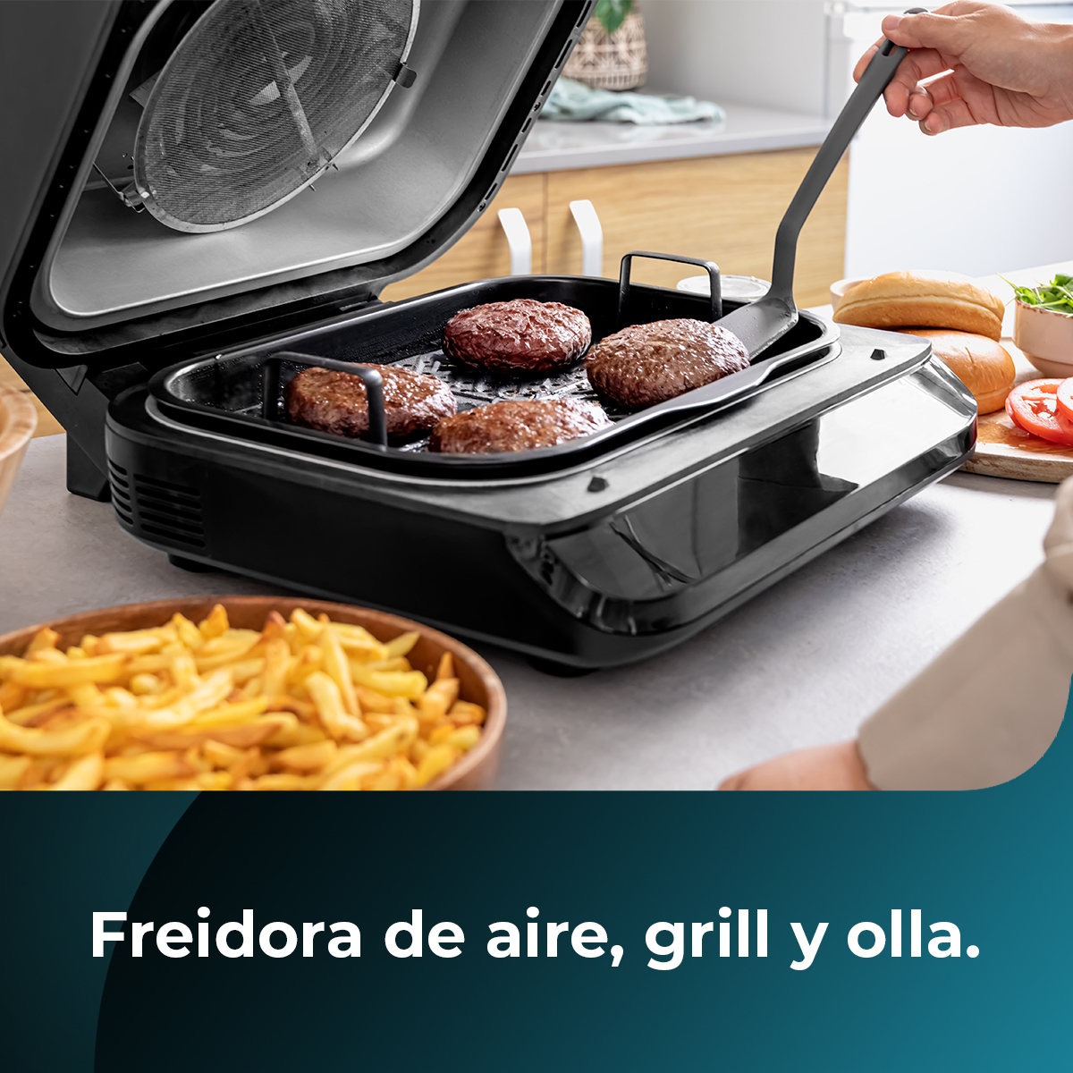 Una friggitrice ad aria sta grigliando hamburger. Patatine fritte e panini per hamburger sono a lato. Una mano tiene una spatola.