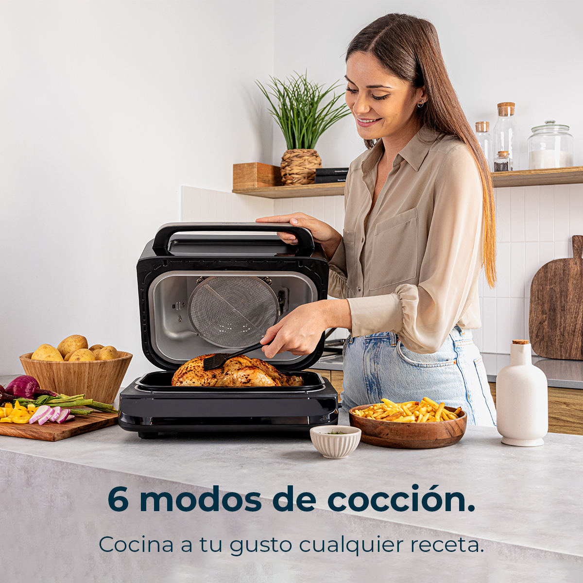 Una donna cucina pollo in una friggitrice ad aria nera. Verdure e patatine fritte sul bancone. Il testo dice '6 modalità di cottura'.