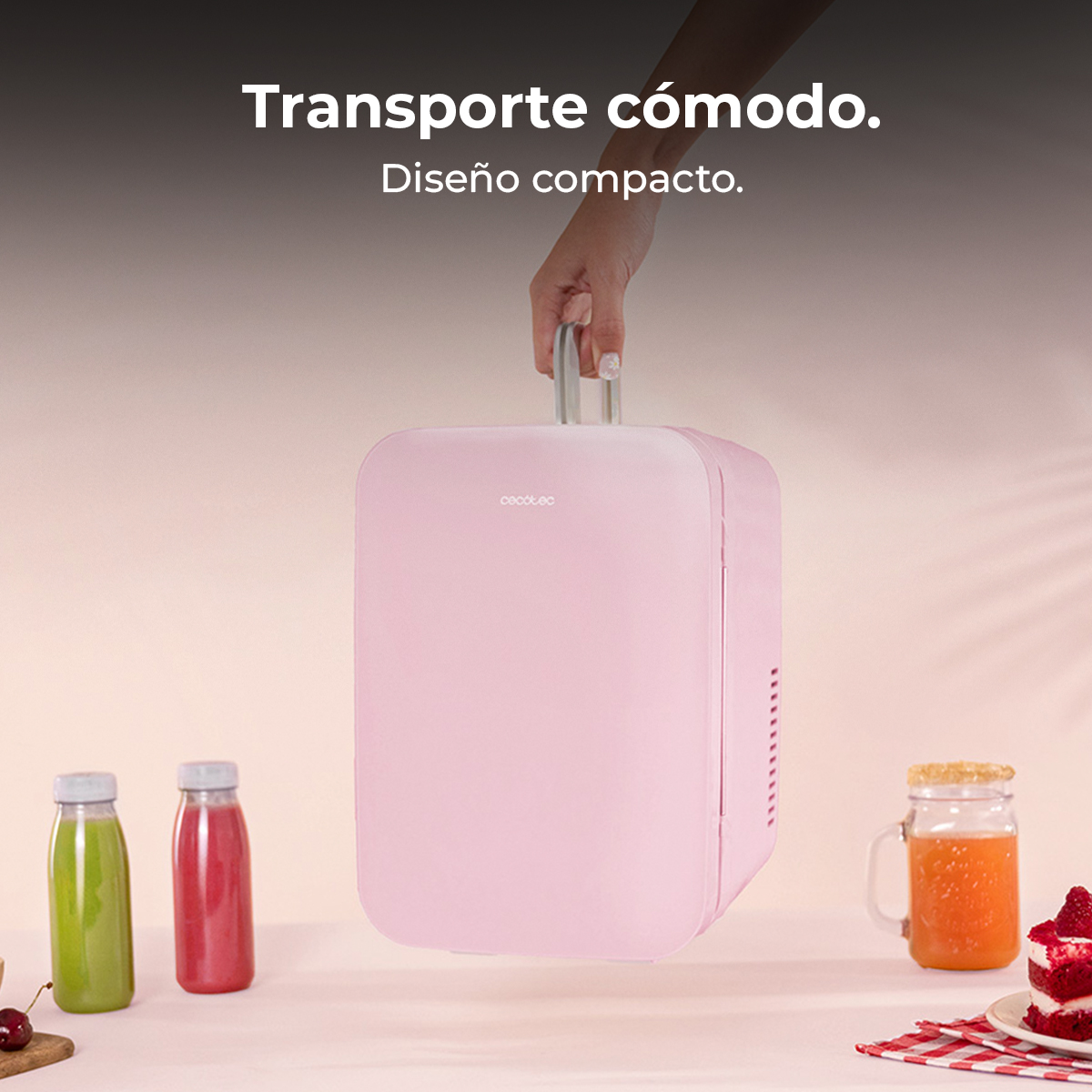 Ręka trzyma różową mini-lodówkę. Butelki z sokiem i ciasto na stole. Tekst: Wygodny transport. Kompaktowy design.