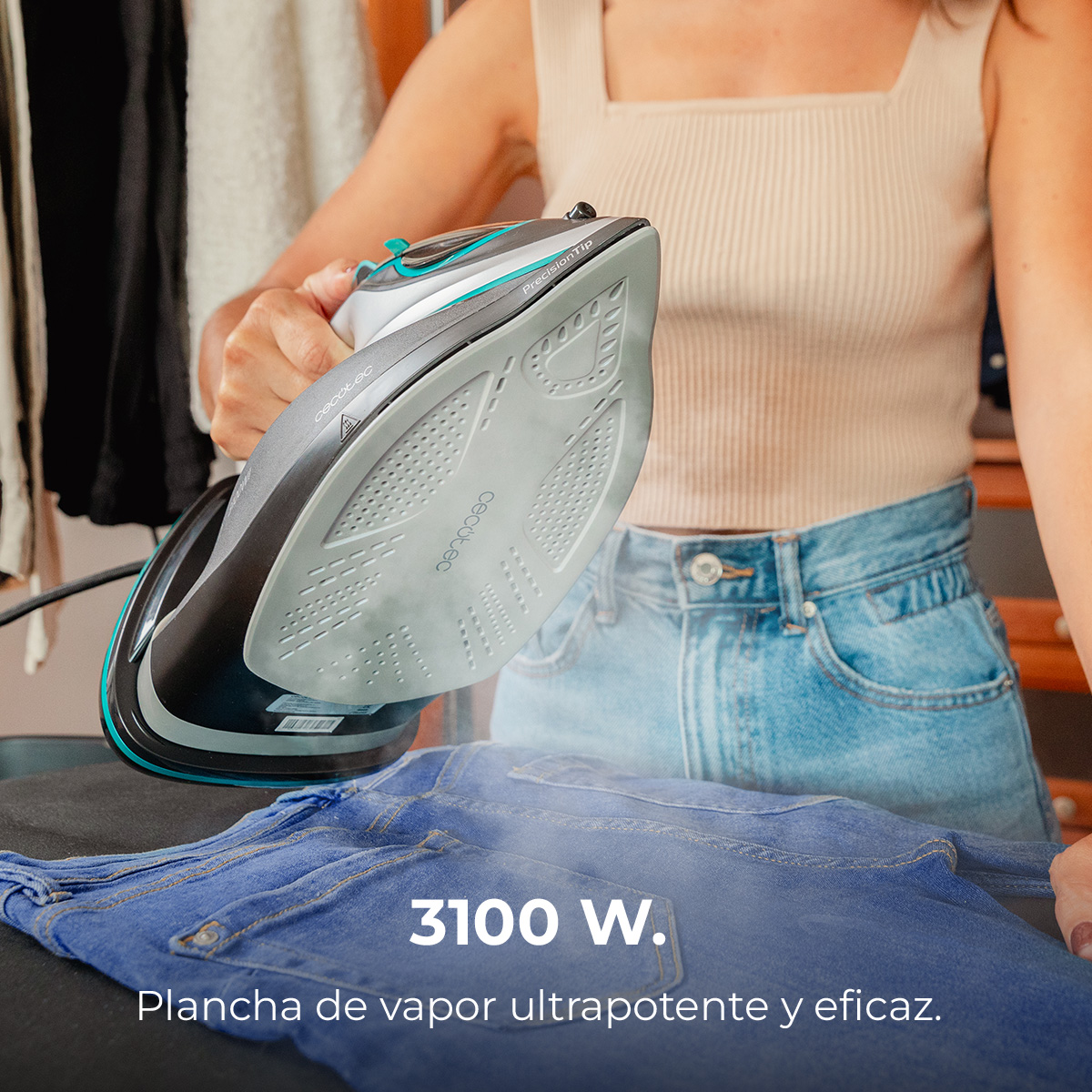Eine Frau bügelt blaue Jeans mit einem Dampfbügeleisen. Das Bügeleisen ist schwarz, grau und türkis. Dampf steigt von der Jeans auf.