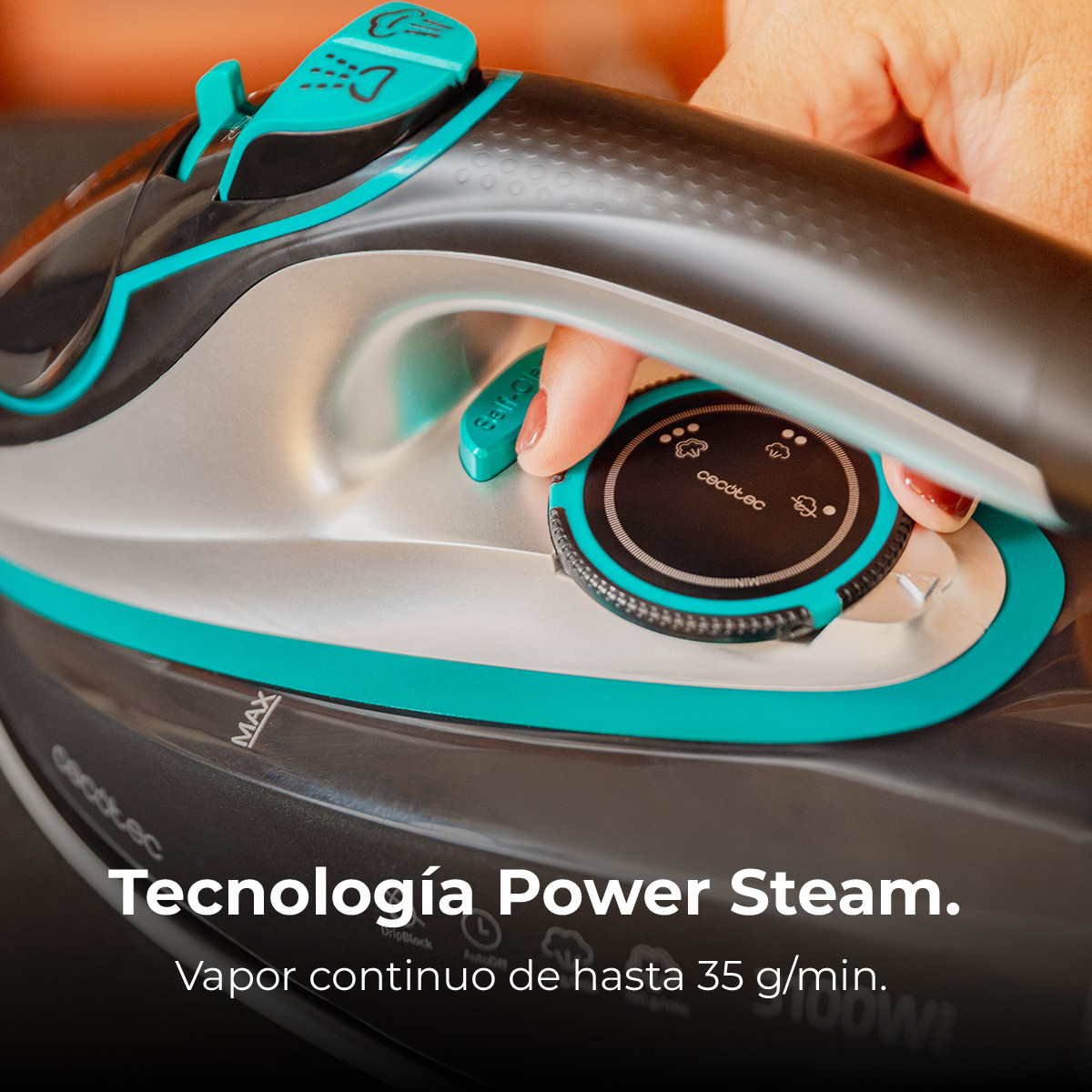 Eine Hand stellt den Drehregler eines schwarz-türkisfarbenen Bügeleisens ein. Der Text lautet 'Tecnología Power Steam' und 'Vapor continuo de hasta 35 g/min.'