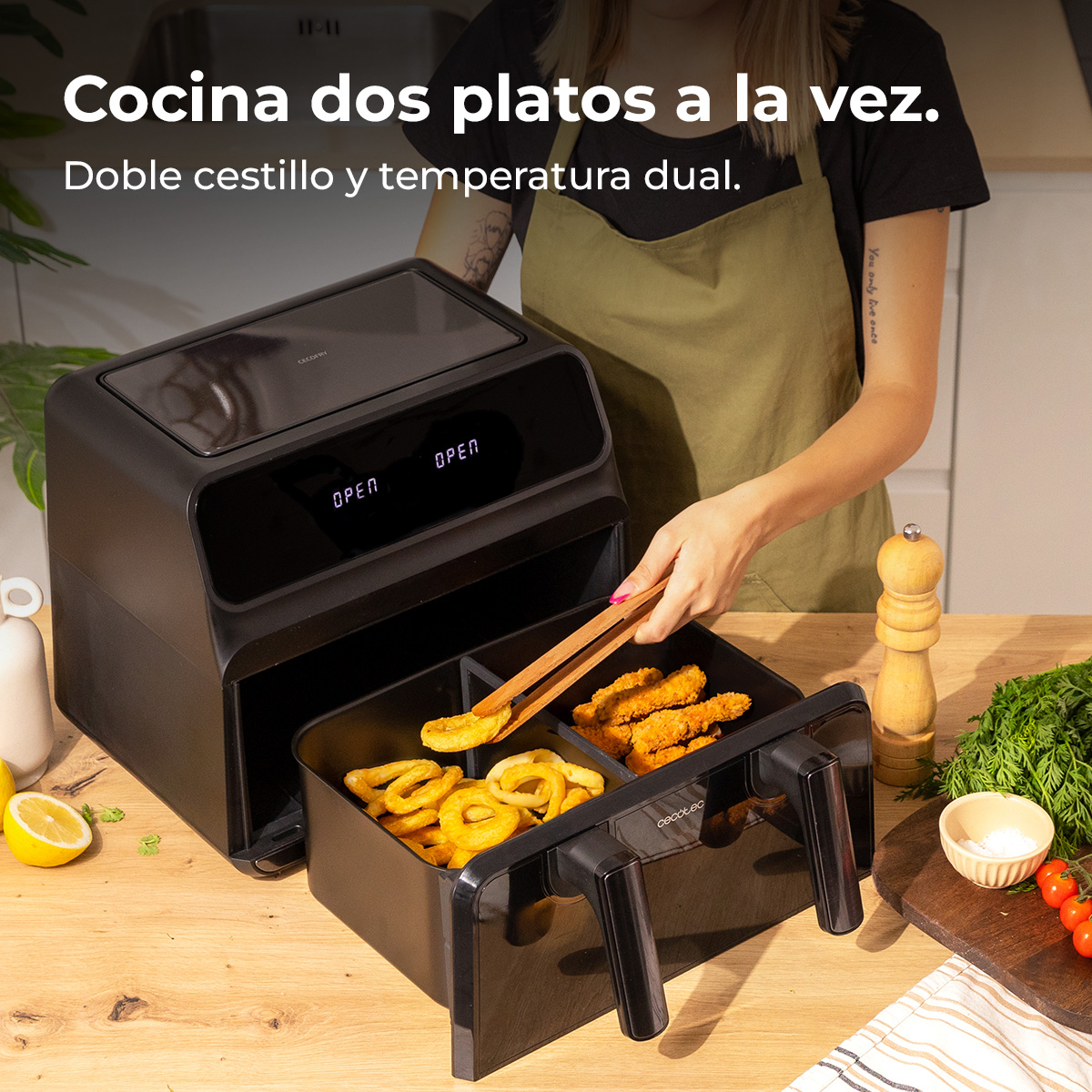 Kobieta używa szczypiec do wyjmowania smażonego jedzenia z czarnej frytownicy powietrznej. Frytownica ma dwa kosze. W pobliżu znajdują się inne produkty spożywcze i składniki.