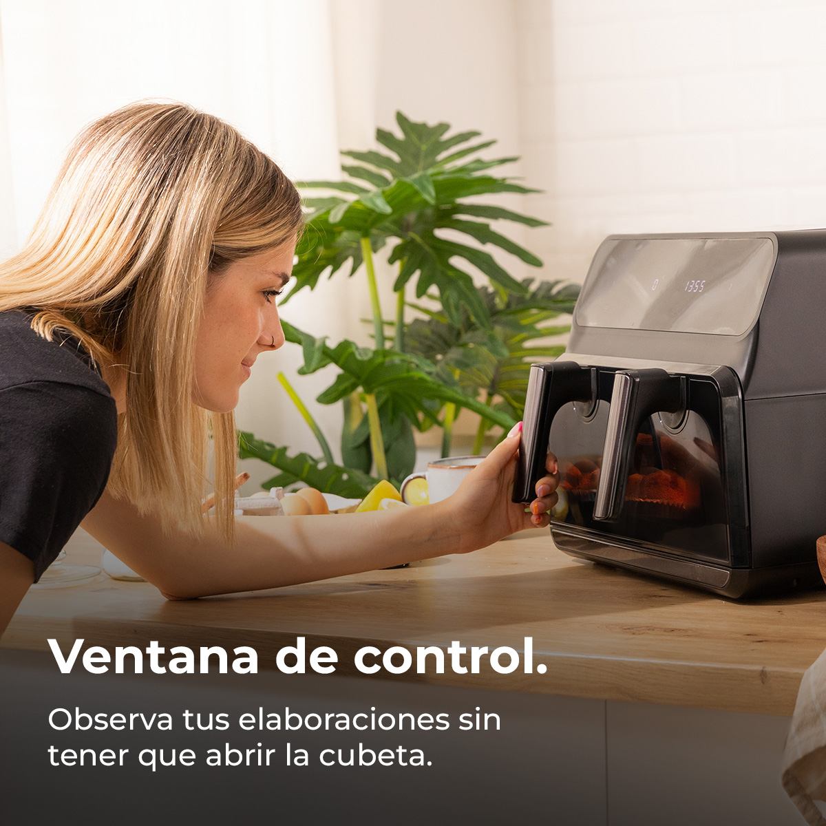 Kobieta patrzy na czarną frytkownicę beztłuszczową. Widoczny jest panel sterowania. W środku gotują się warzywa. W tle roślina.