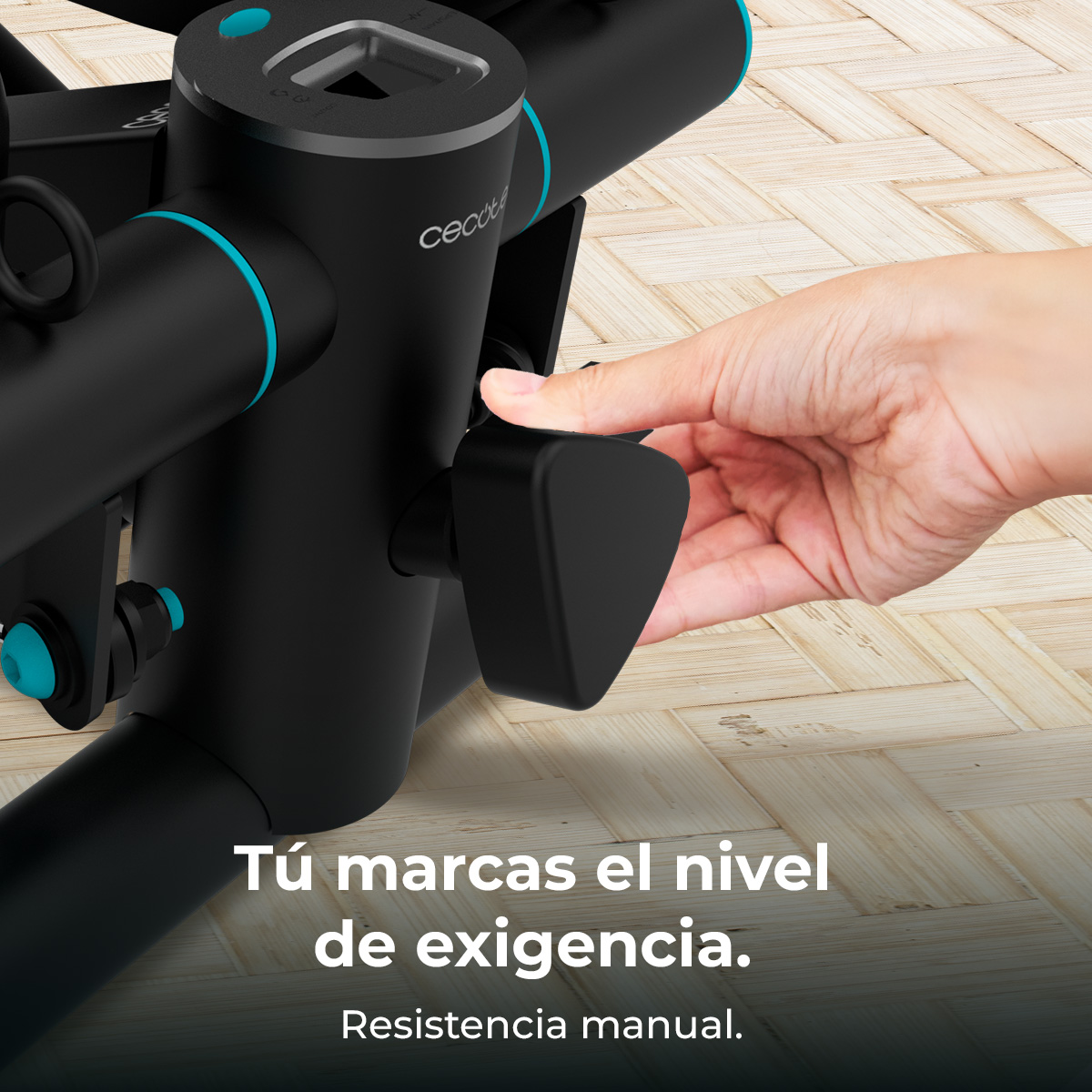 Una mano ajusta una perilla de resistencia negra en una bicicleta estática. La bicicleta es negra con detalles turquesa, sobre un suelo de madera.