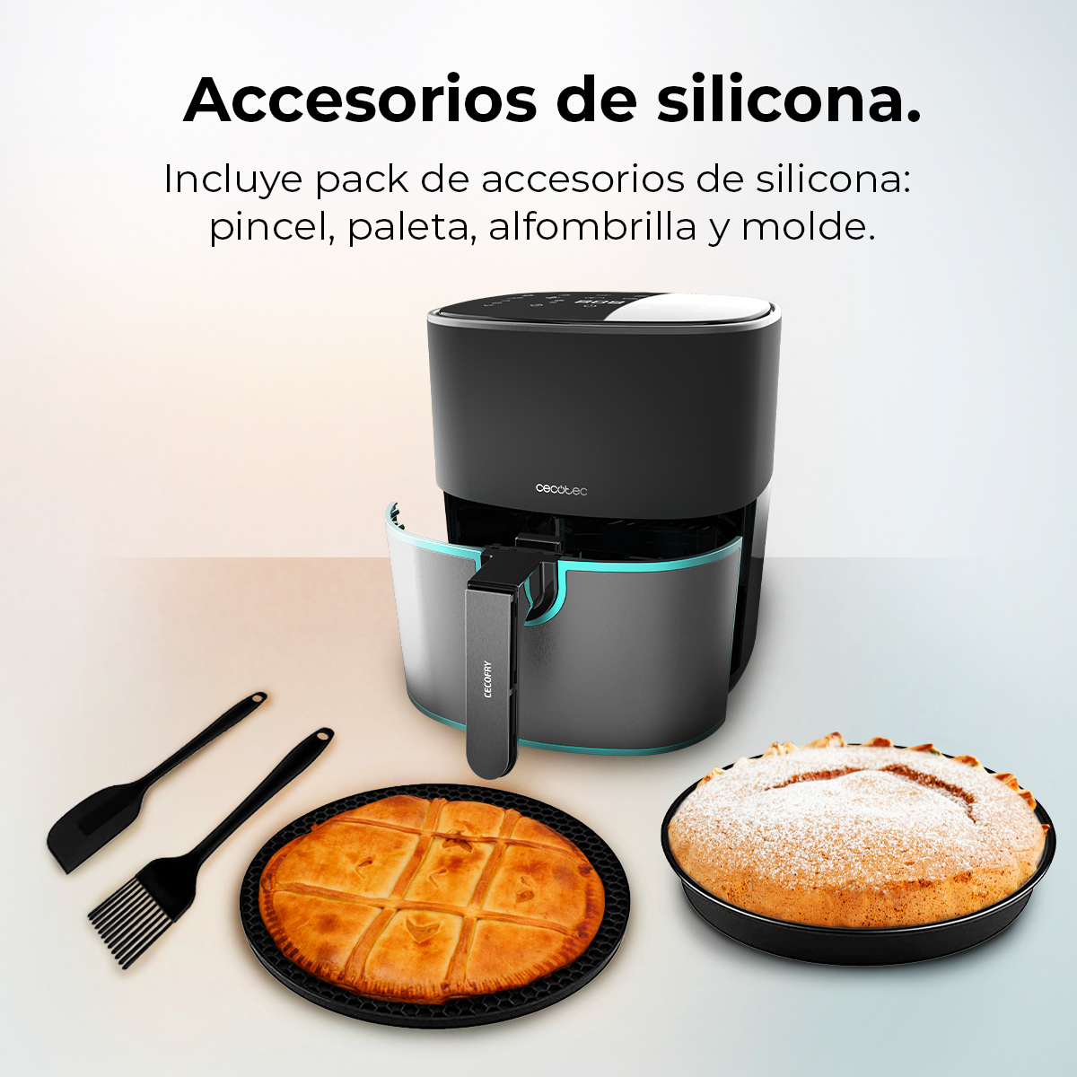 Una freidora de aire con accesorios de silicona: brocha, espátula, alfombrilla y molde. Dos tartas están al lado.