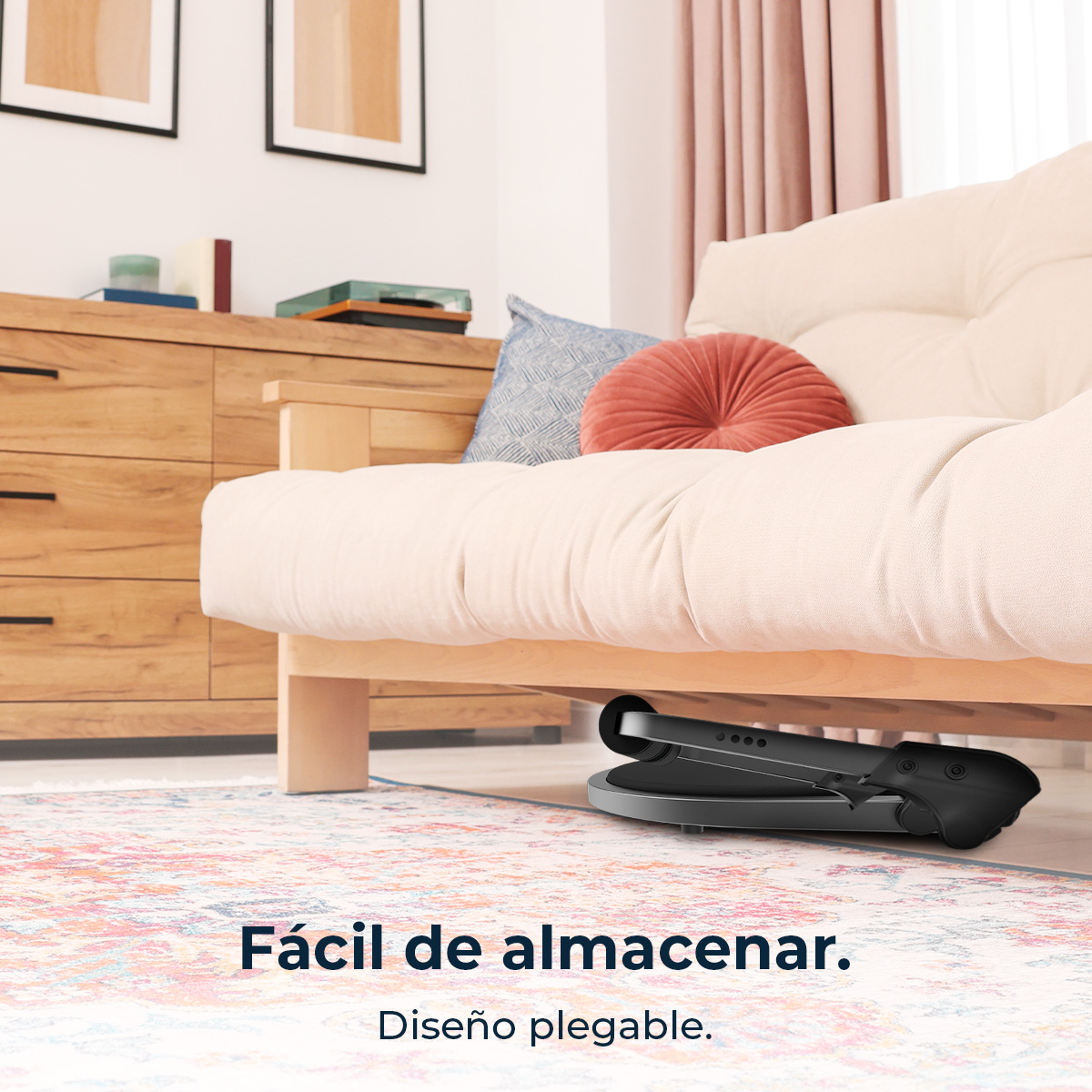 Un divano futon color crema è sopra un tappeto. Un dispositivo nero è sotto il divano. Lo sfondo include un mobile in legno e tende rosa.
