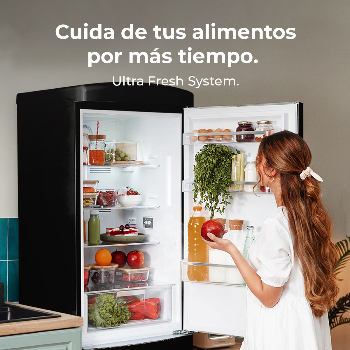 Kobieta z jabłkiem patrzy na lodówkę pełną jedzenia. Drzwi lodówki są otwarte, pokazując owoce, warzywa i napoje.