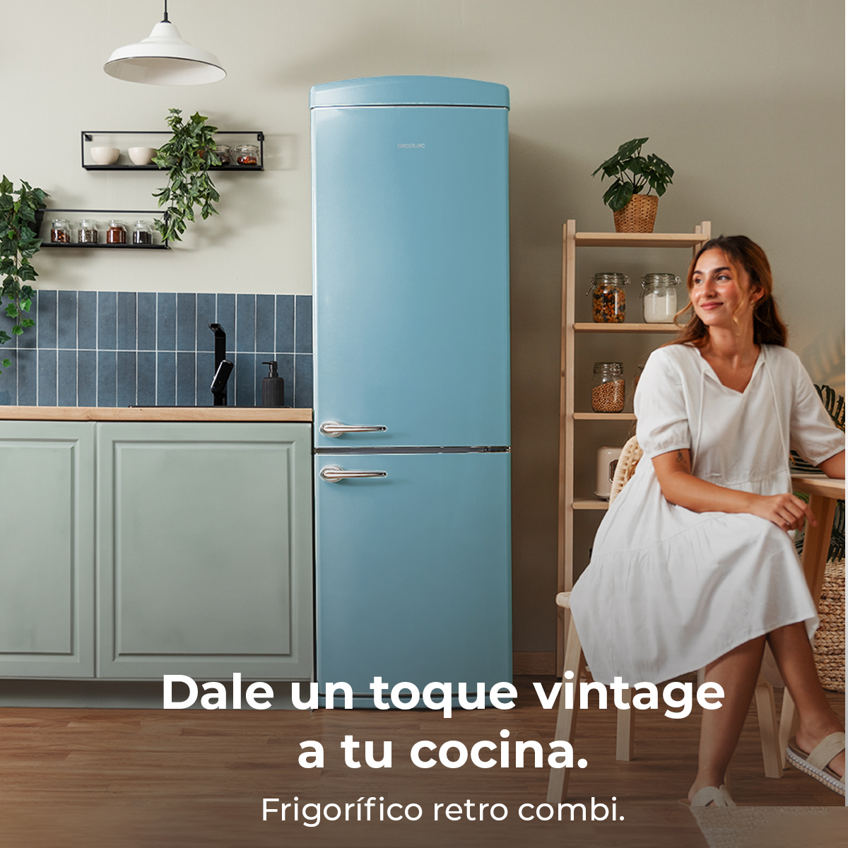 Kobieta siedzi obok niebieskiej lodówki retro. Kuchnia ma rośliny, półki i drewniany stół. Tekst: 'Nadaj swojej kuchni charakteru vintage'.