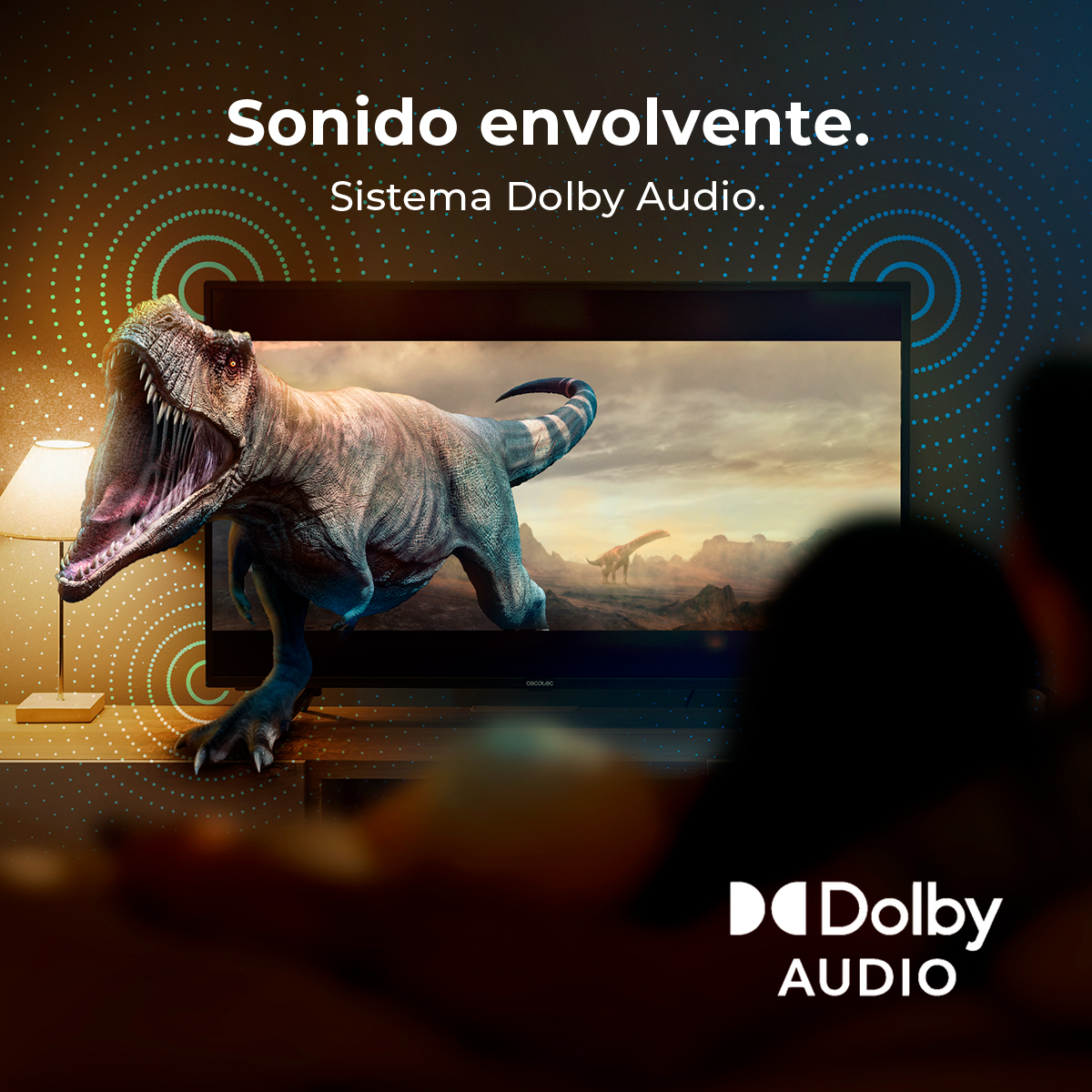 Telewizor pokazuje scenę z dinozaurami. Telewizor jest w salonie, z logo Dolby Audio na dole. Tekst mówi 'Sonido envolvente'.