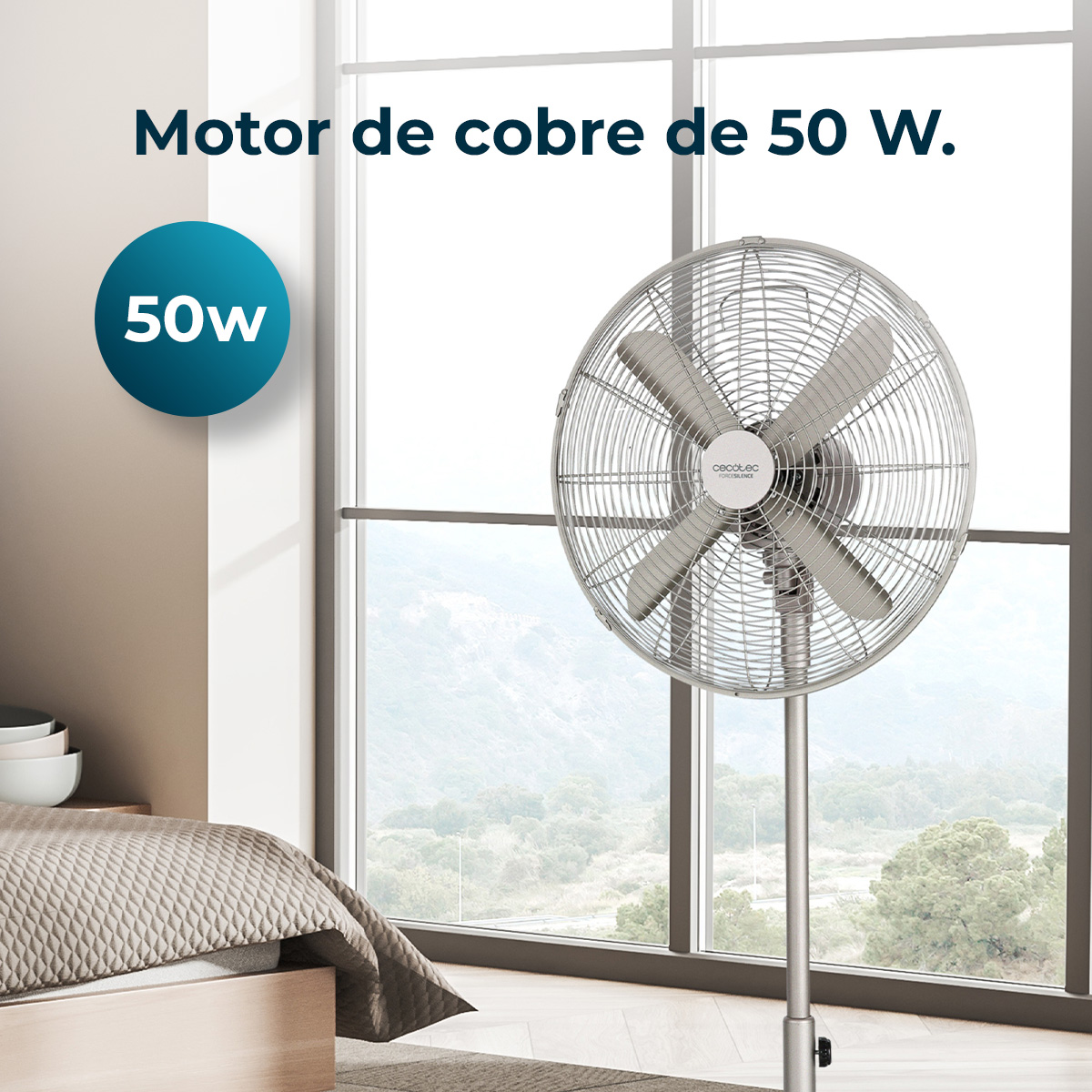 Metalowy wentylator w pokoju. Okno z widokiem na góry. Tekst: silnik miedziany 50W. Łóżko po lewej.