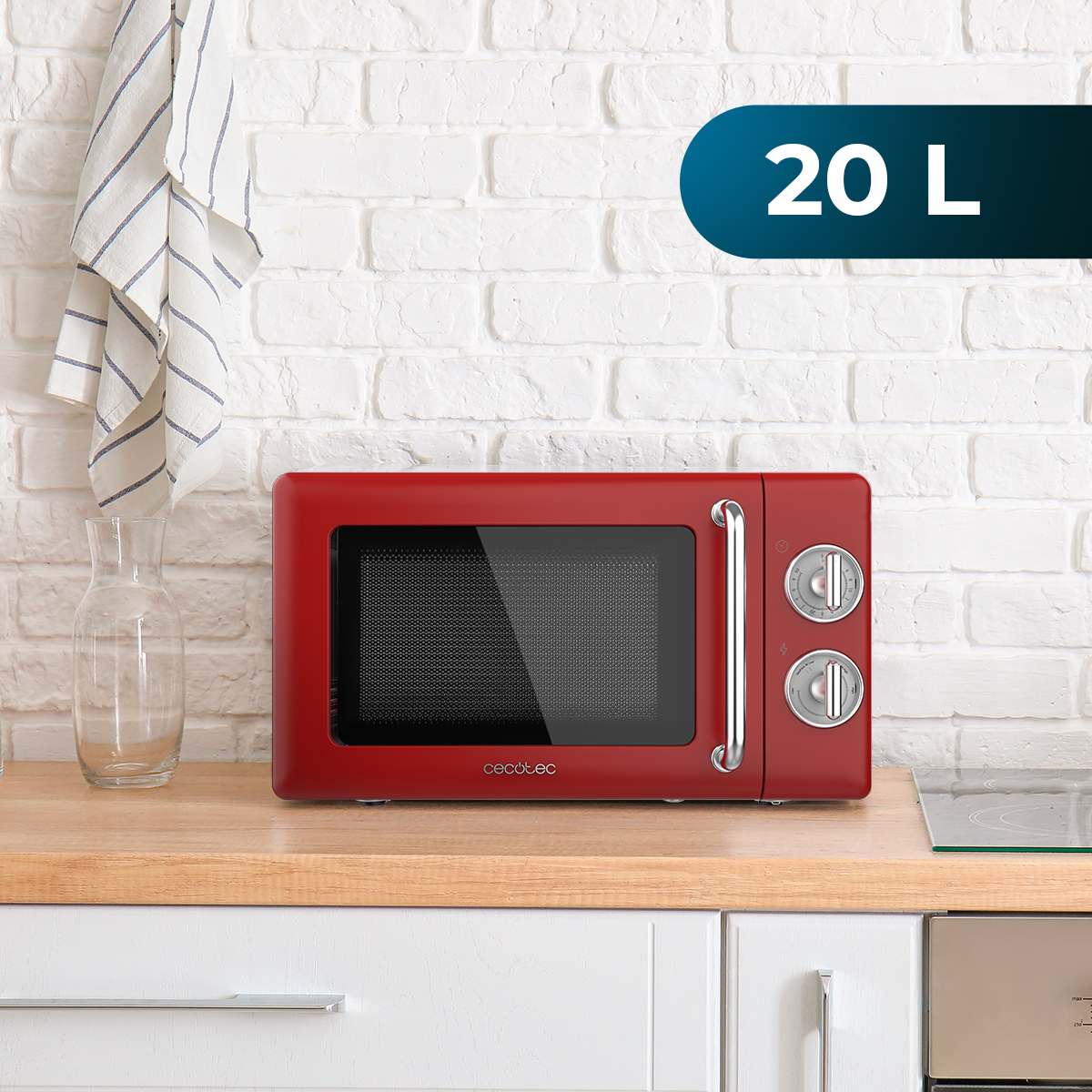 Czerwona kuchenka mikrofalowa na drewnianym blacie. Szklana karafka i biały ręcznik wiszą na ceglanej ścianie.