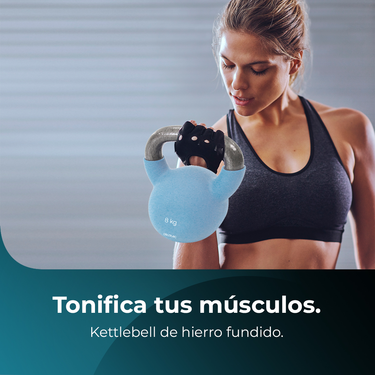 Una mujer sostiene una pesa rusa azul de 8 kg. Lleva un sujetador deportivo negro y guantes. El fondo es una pared borrosa con texto.