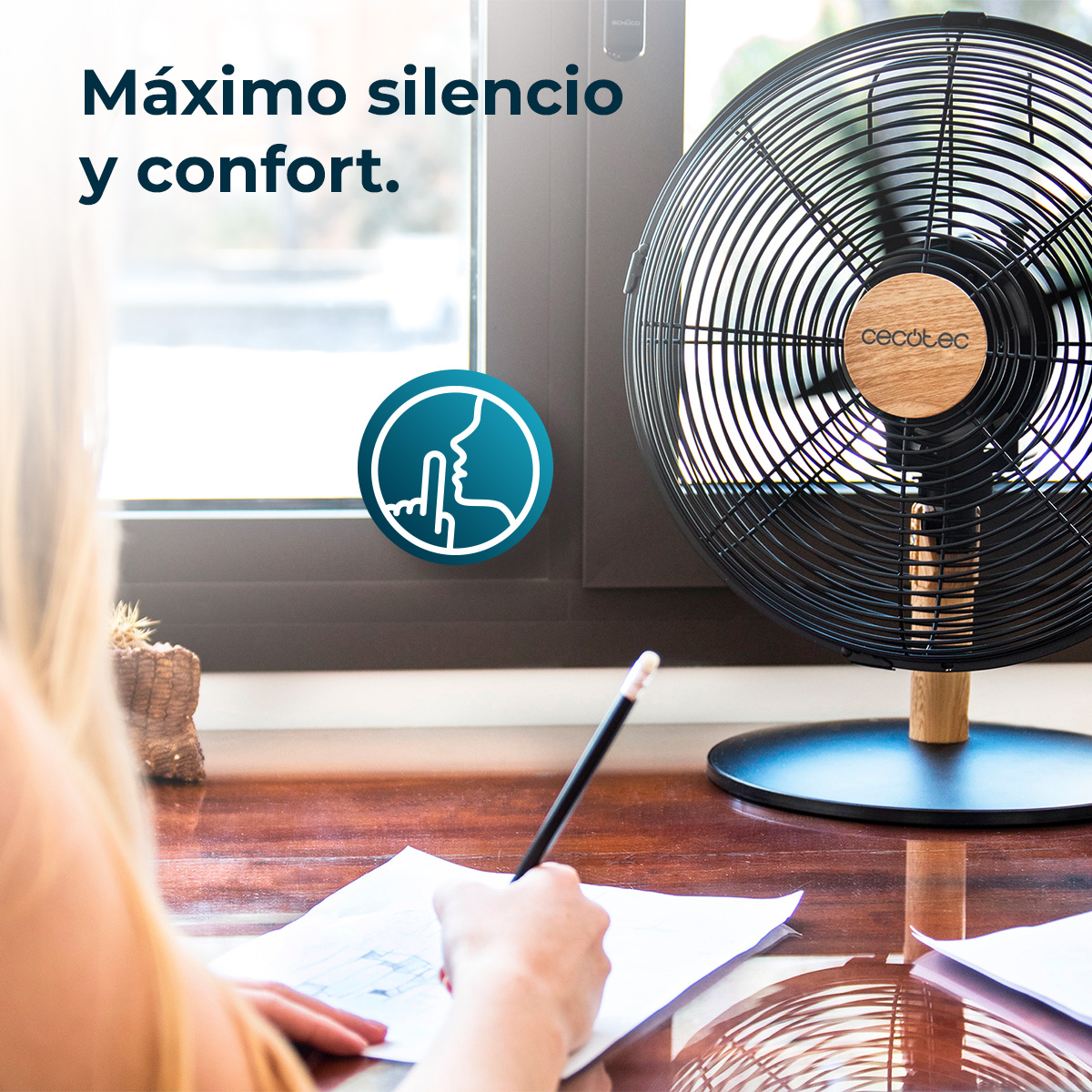 Kobieta rysuje na biurku z wentylatorem. Wentylator jest czarny, łopatki się obracają. Niebieska ikona wskazuje ciszę.