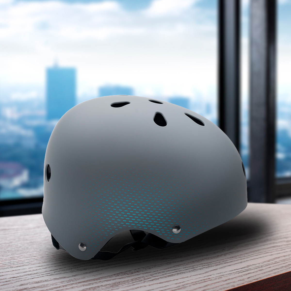 Un casco gris con un patrón de puntos azules está sobre una superficie de madera. Se ve un paisaje urbano borroso a través de una ventana.