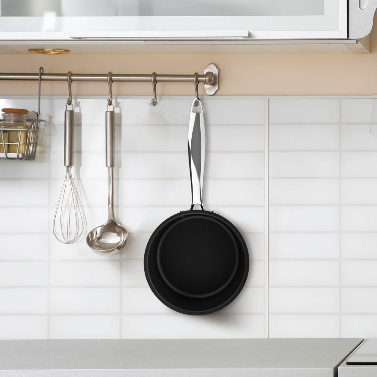 Escena de cocina con utensilios colgantes: batidor, cucharón y sartén. Pared de azulejos blancos con estante metálico. Encimera clara.