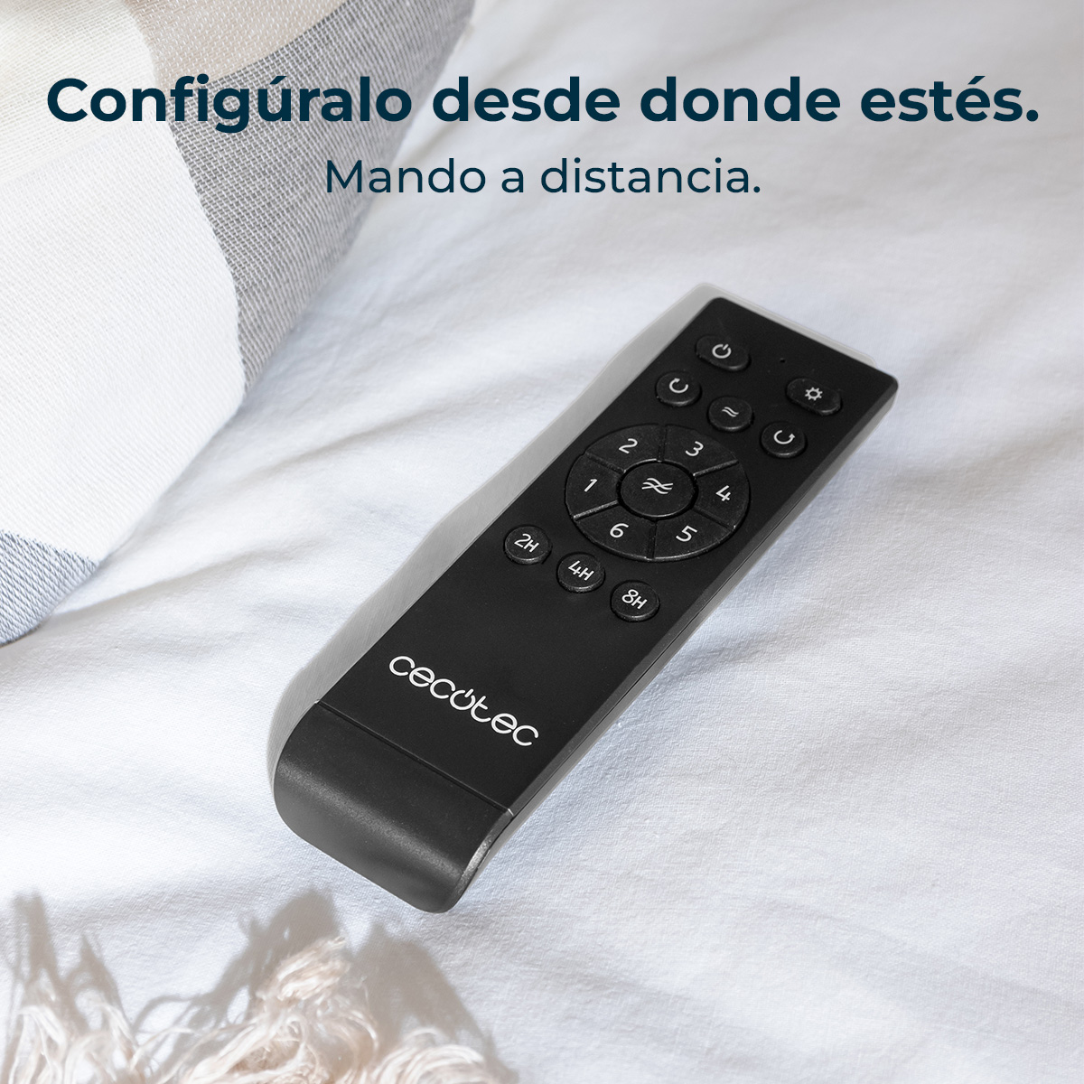 Un telecomando nero su un lenzuolo bianco. Ha pulsanti e un marchio. Un cuscino a scacchi è sullo sfondo.