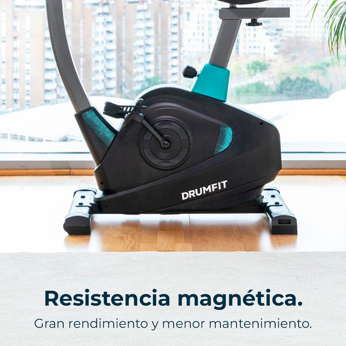 Una cyclette nera con dettagli blu, etichettata 'DRUMFIT', su un tappeto. Sullo sfondo una finestra con vista sulla città.