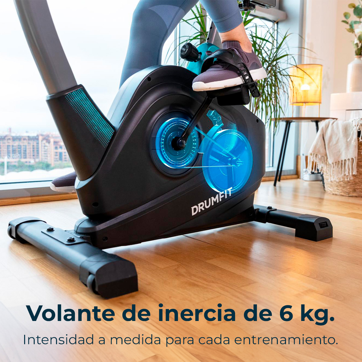 Una persona usa una cyclette DRUMFIT nera. Il volano è evidenziato. Il testo sottostante dice 'Volano da 6 kg'.