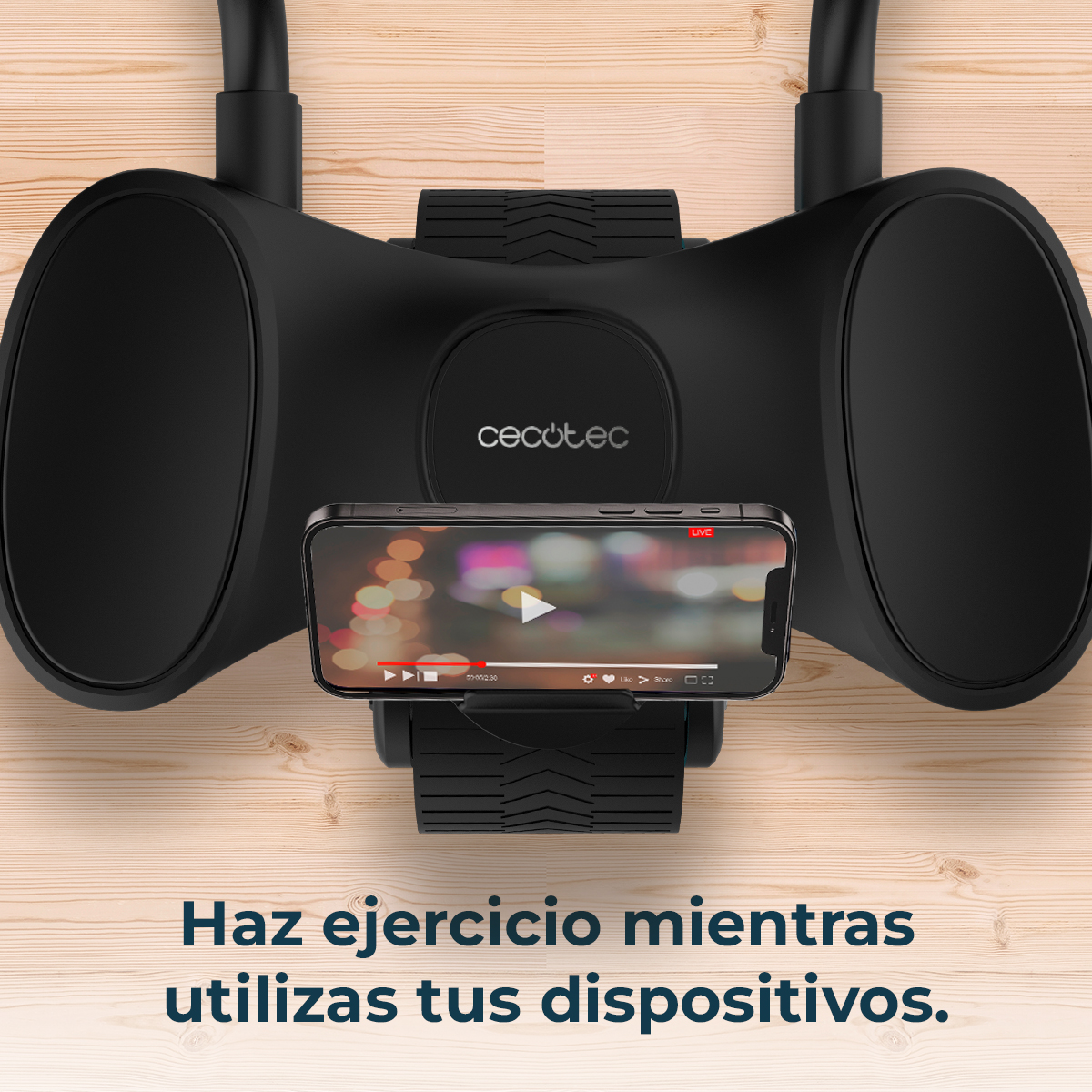 Dispositivo per esercizi nero con telefono che mostra un video. Il dispositivo è su legno, con testo spagnolo sotto.