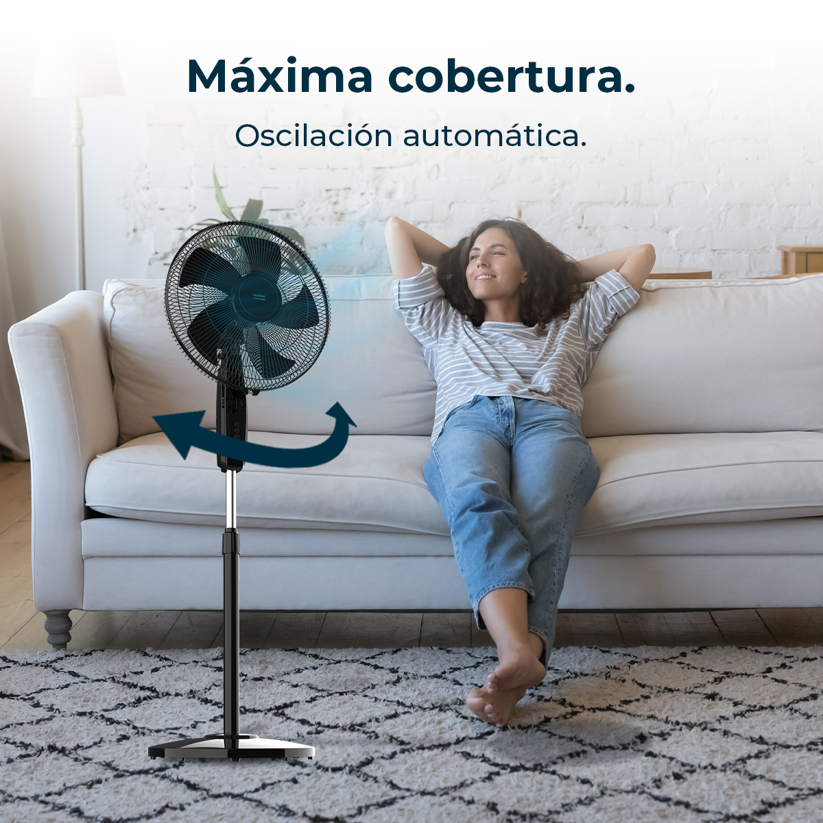 Una donna si rilassa su un divano mentre un ventilatore soffia aria. Il ventilatore è nero e poggia su una base nera.