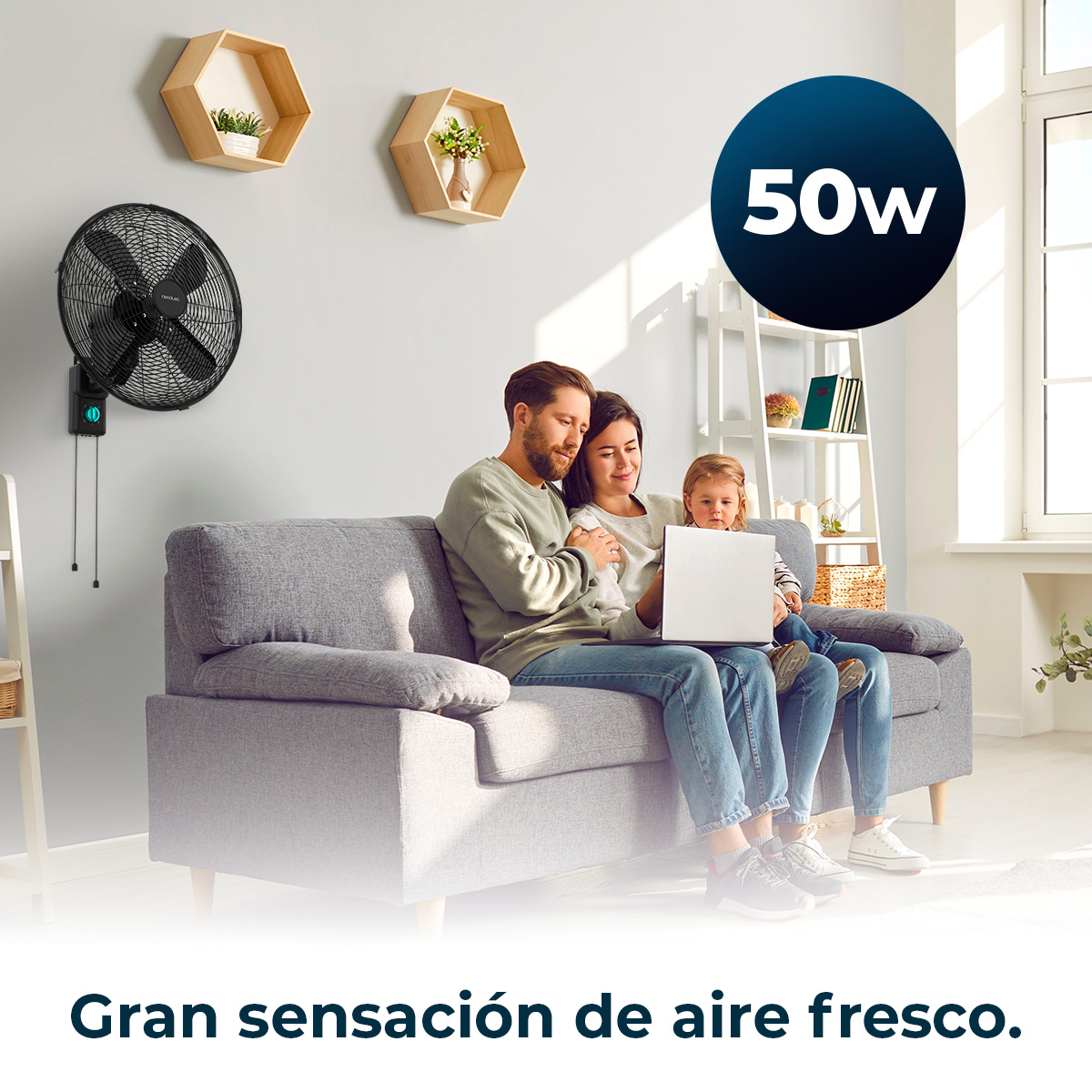 Familie auf einem Sofa mit Laptop, Wandventilator und 50W Text. Der Text 'Gran sensación de aire fresco' steht unten.