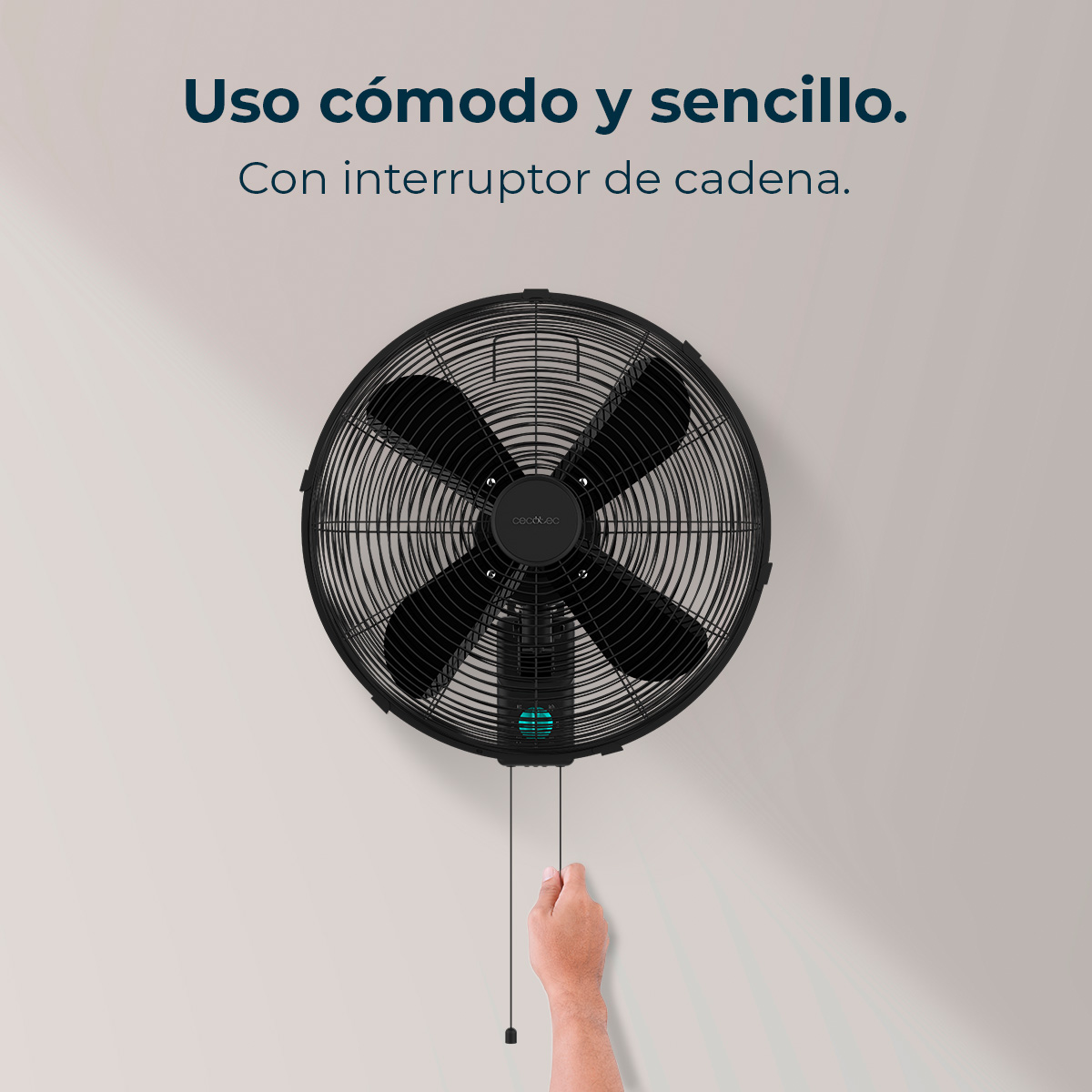 Ein schwarzer, an der Wand befestigter Ventilator mit vier Flügeln, eine Hand, die an der Schnur zieht. Der Ventilator ist an einer hellgrauen Wand.