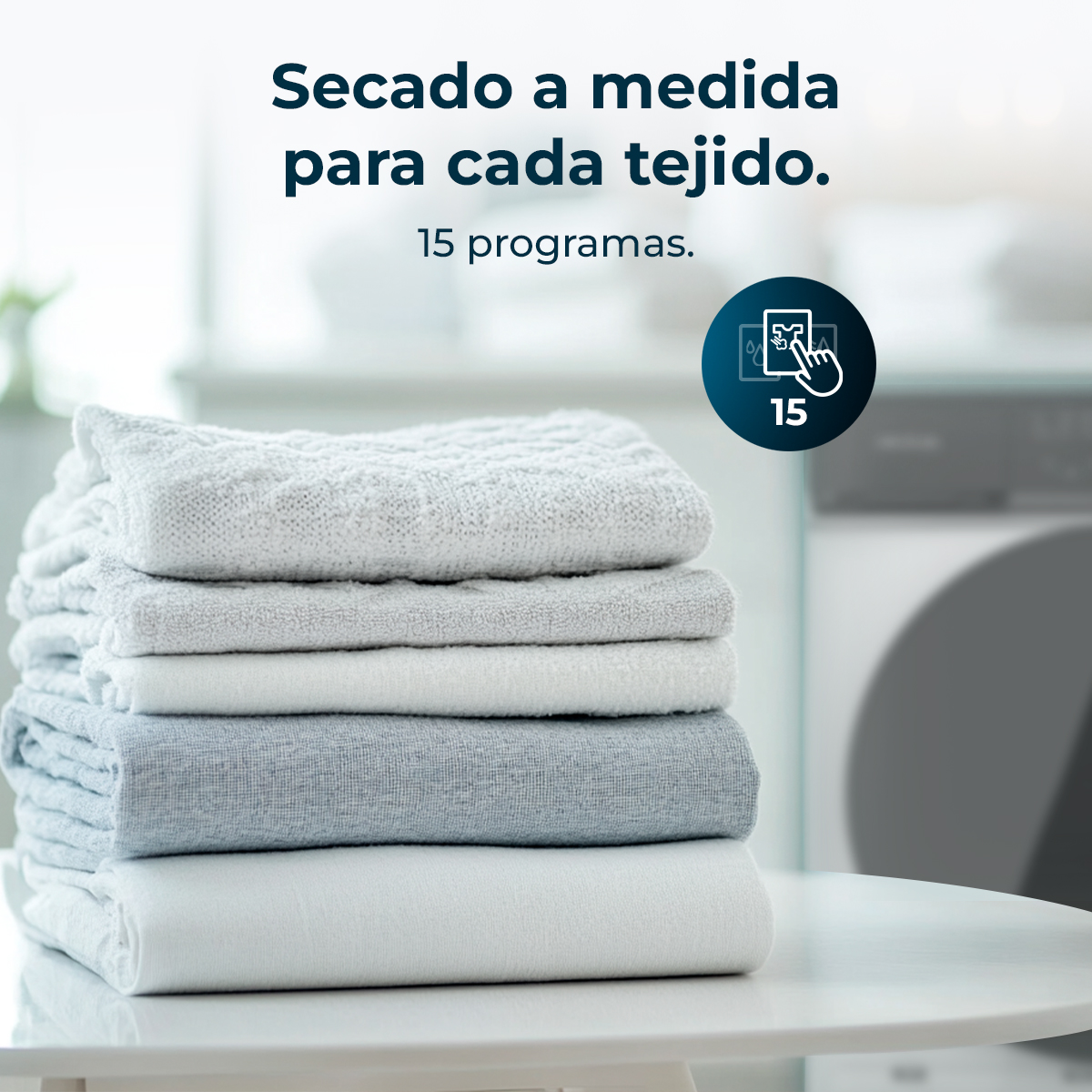 Una pila de toallas dobladas en tonos blancos y grises sobre una mesa blanca. El texto superior dice 'Secado a medida para cada tejido'.