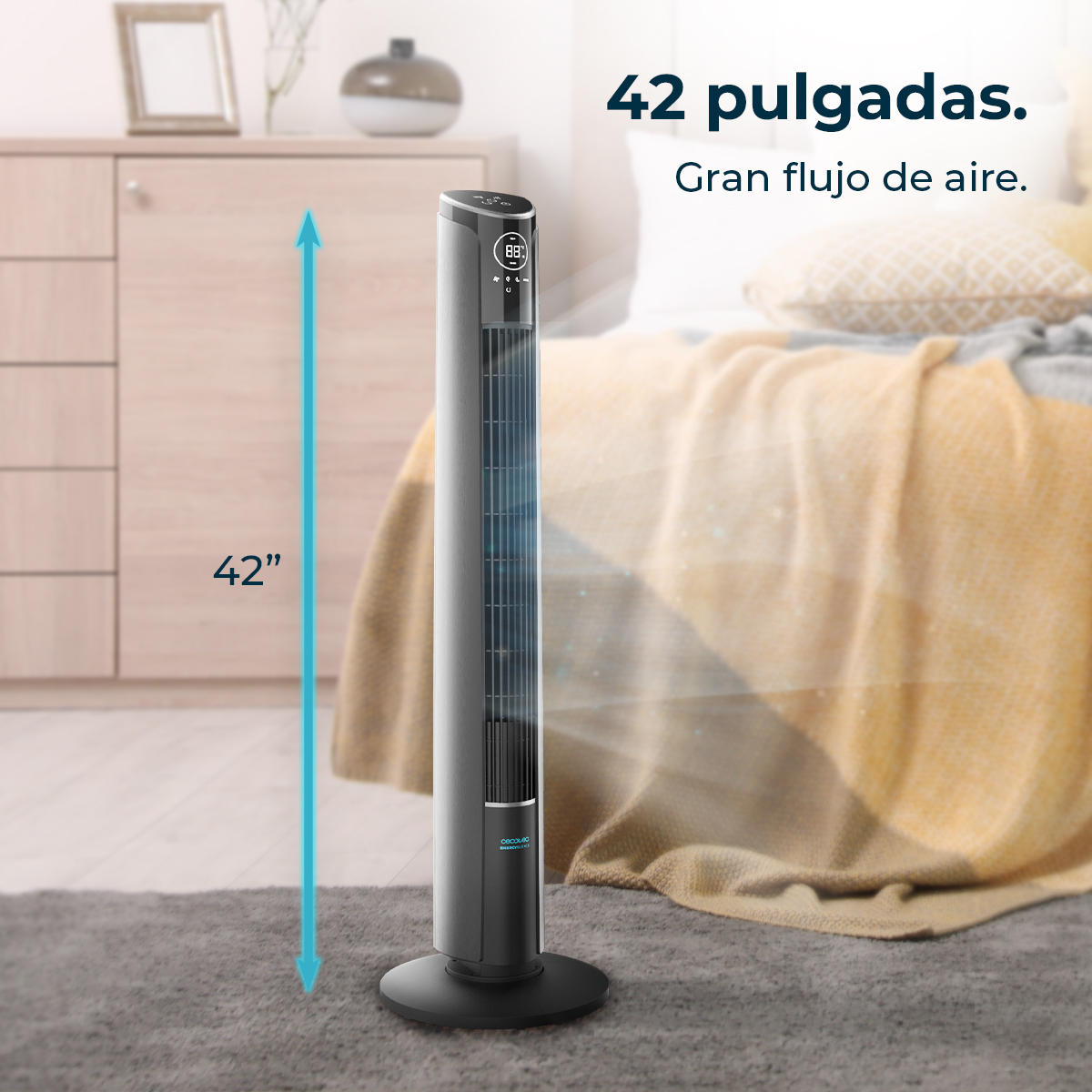 Un ventilador de torre gris está en una habitación. Mide 42 pulgadas de alto. Una cama con una manta amarilla está en el fondo. El ventilador tiene una pantalla digital.