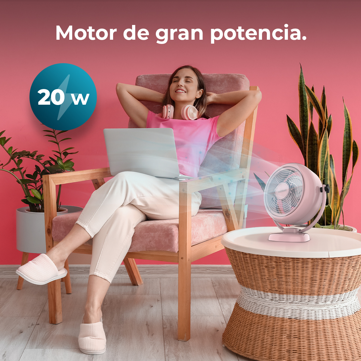 Una donna si rilassa su una sedia con un laptop, accanto a un ventilatore rosa. Un cartello da 20w e testo sono sullo sfondo.