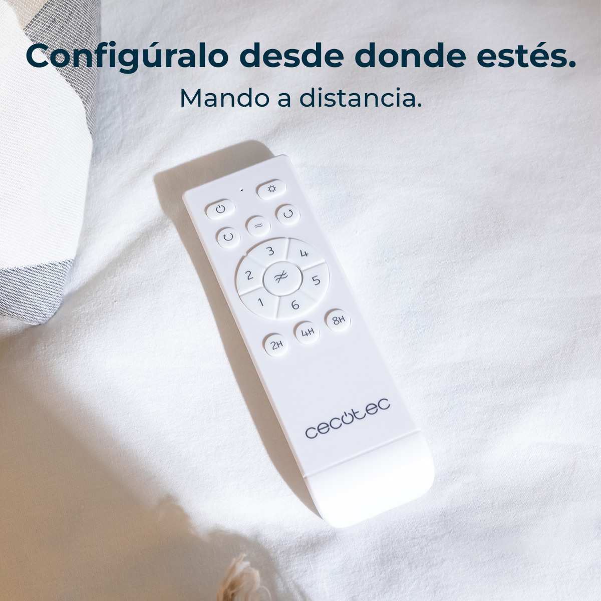 Un telecomando bianco su lenzuola bianche. Il telecomando ha pulsanti e numeri, con il marchio 'cecotec' in basso.
