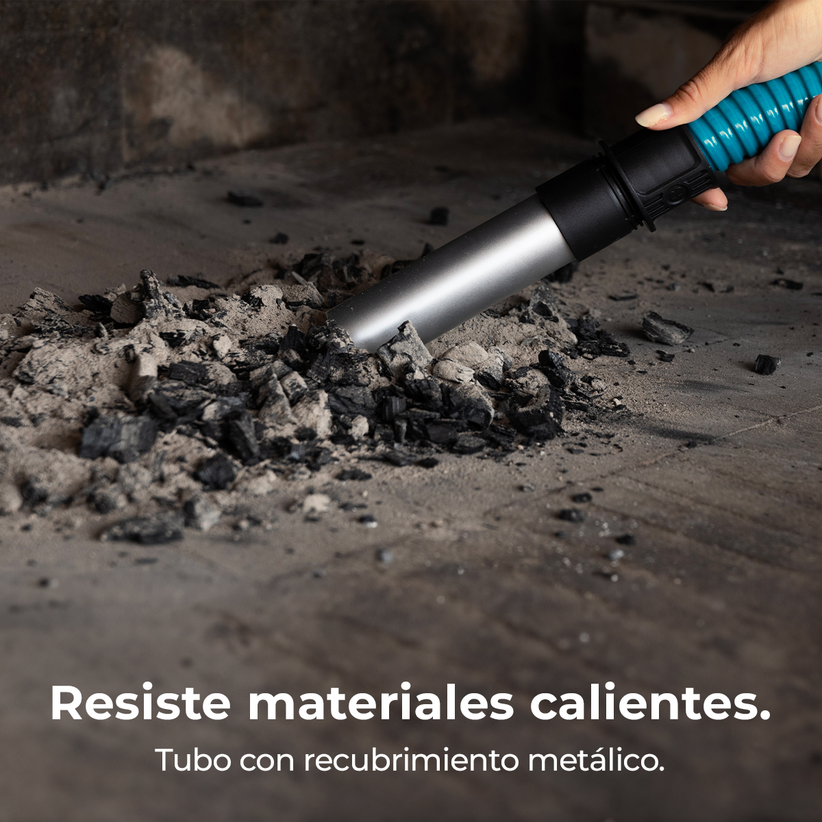 Una mano tiene un tubo blu collegato a un tubo aspirapolvere argentato che pulisce cenere e carbone da una superficie.