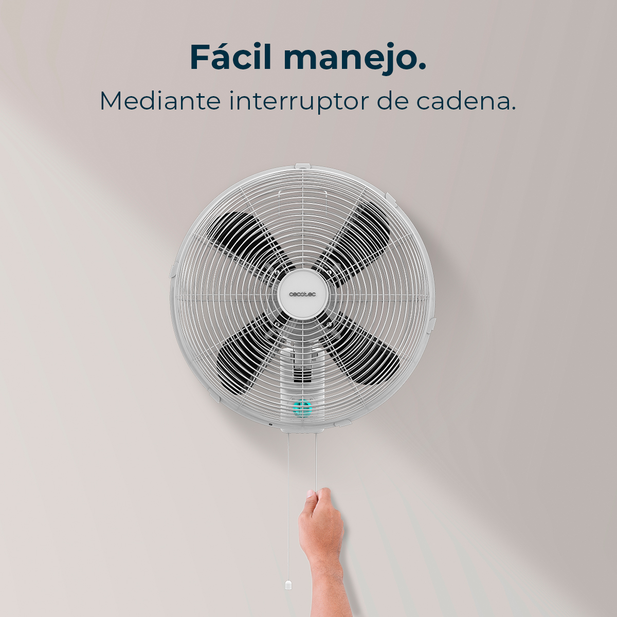 Un ventilador de pared blanco con aspas negras está colgado en una pared clara. Una mano tira de un cordón conectado al ventilador.