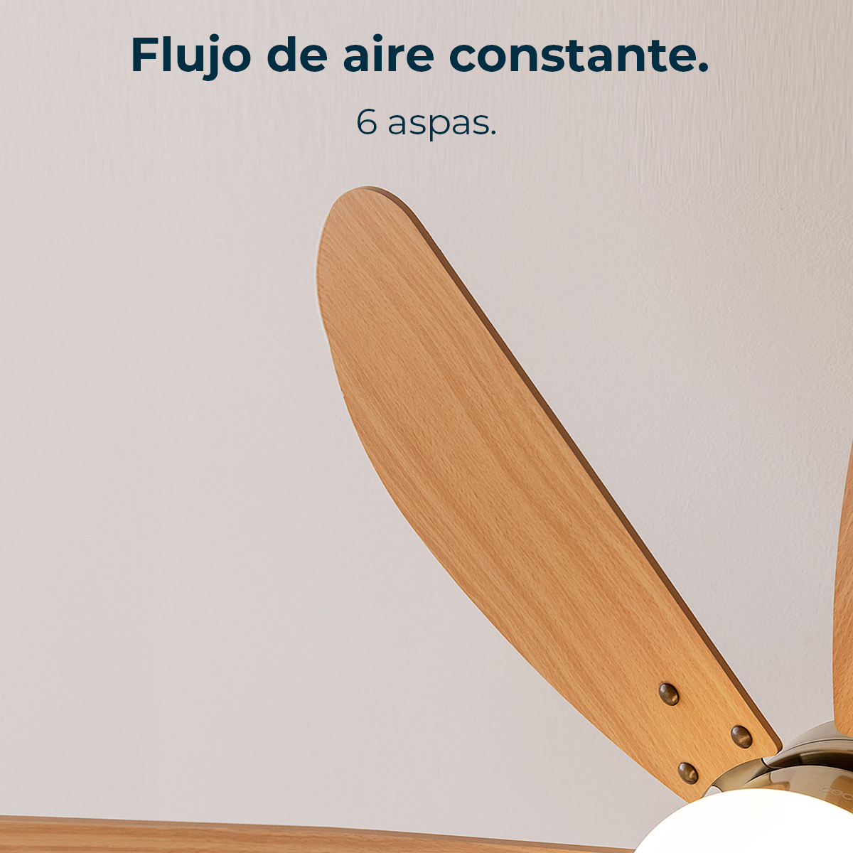 Primo piano di un ventilatore a soffitto in legno con sei pale. Lo sfondo mostra un muro bianco con testo in spagnolo.