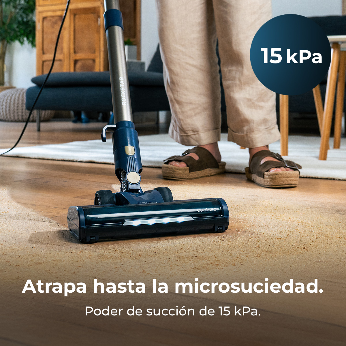 Una persona aspira una alfombra con una aspiradora azul y plateada. La aspiradora dice 'ROCKSTAR'. Un texto dice '15 kPa'.