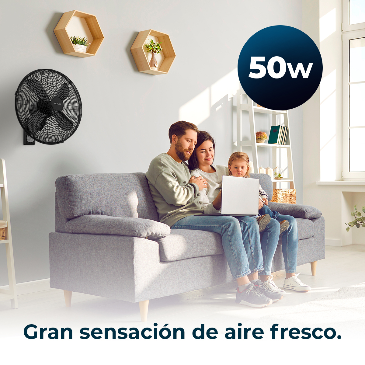 Familia sentada en un sofá, usando una laptop. Un ventilador negro en la pared. El texto dice 'Gran sensación de aire fresco'.