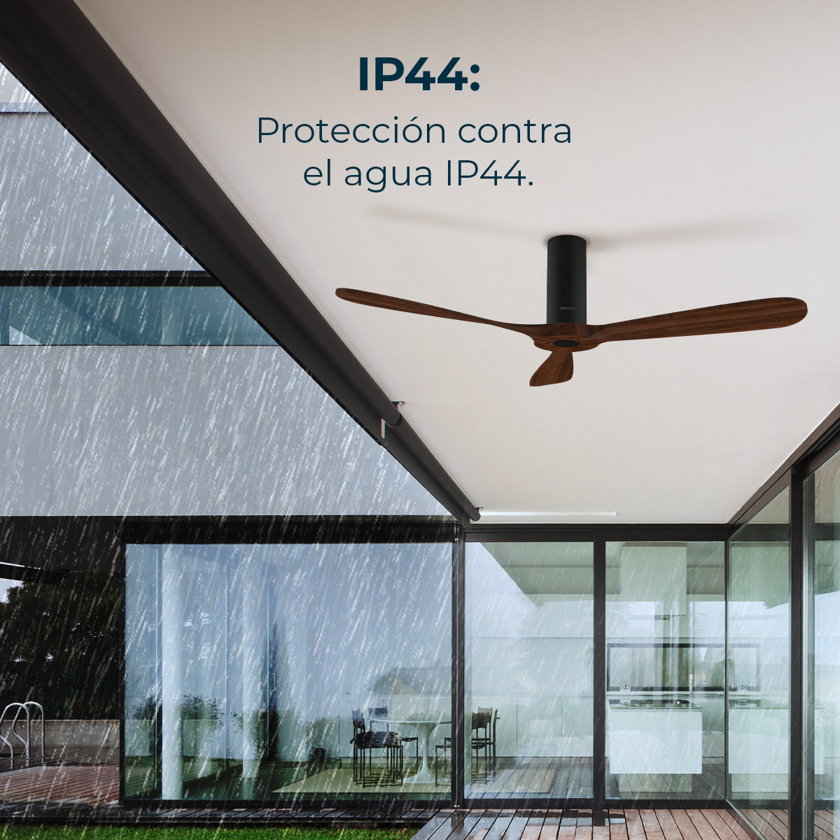 Wentylator sufitowy z drewnianymi łopatkami jest zainstalowany na białym suficie. Deszcz pada na zewnątrz szklanej ściany, z napisem 'IP44: Protección contra el agua IP44.'