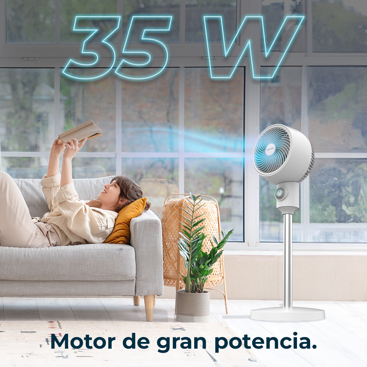 Donna su un divano che legge, vicino a un ventilatore bianco. 35W è scritto sopra. C'è una pianta e una lampada sullo sfondo.