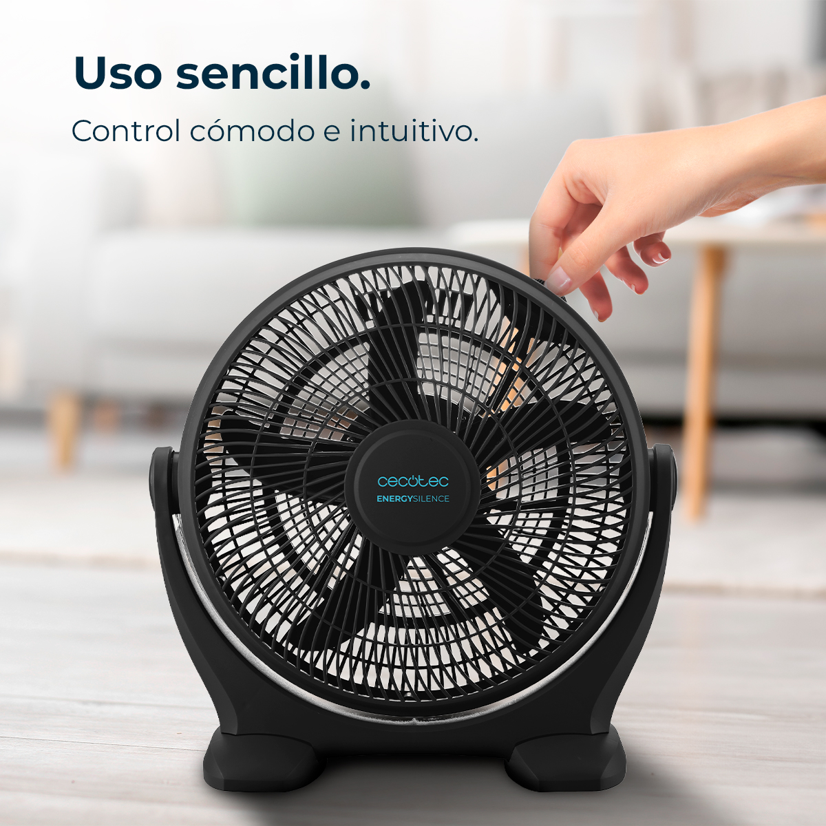 Ein schwarzer Ventilator, der von einer Hand eingestellt wird. Der Ventilator hat einen Käfig und Flügel. Der Hintergrund ist verschwommen.