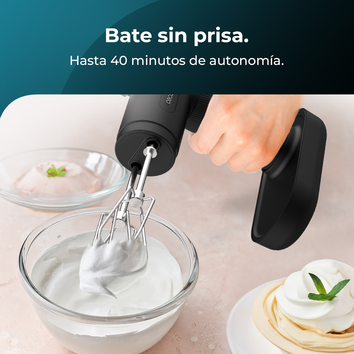Una mano tiene un mixer nero sopra una ciotola di panna montata. Altre ciotole con panna e un dolce sono sullo sfondo.