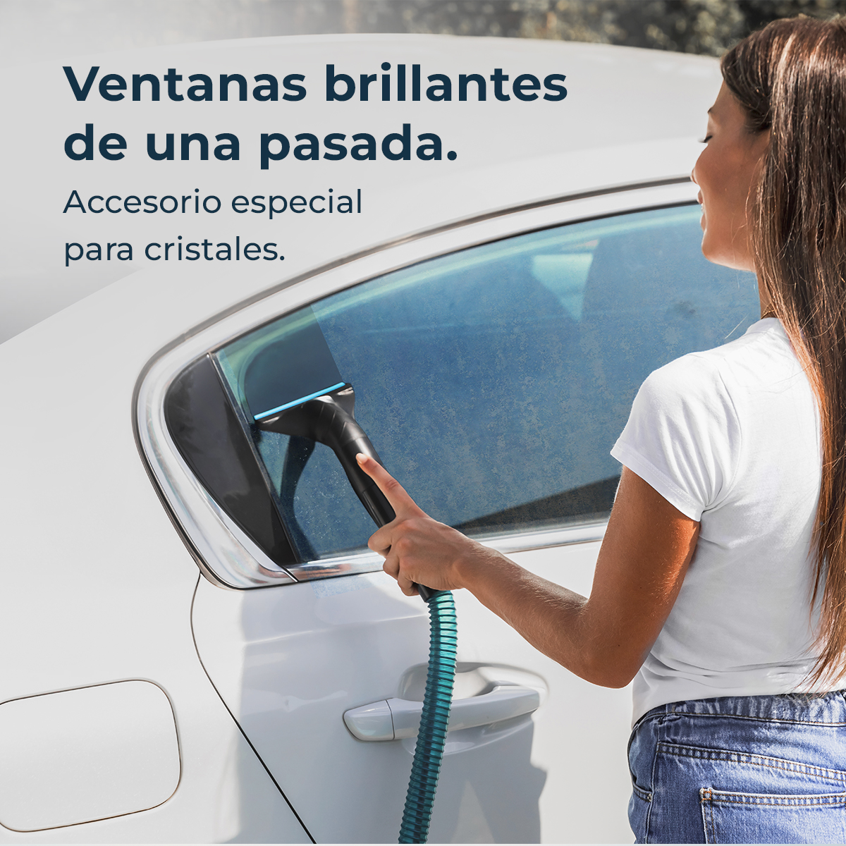 Una mujer limpia la ventana de un coche con una herramienta de limpieza azul y negra. El coche es blanco. El fondo son árboles borrosos.