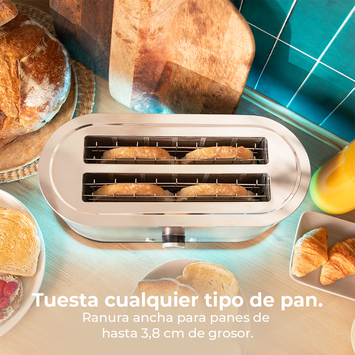 Una tostadora cromada con rebanadas de pan tostado. Al lado, pan, cruasanes y zumo. El fondo tiene una tabla de madera y azulejos turquesa.