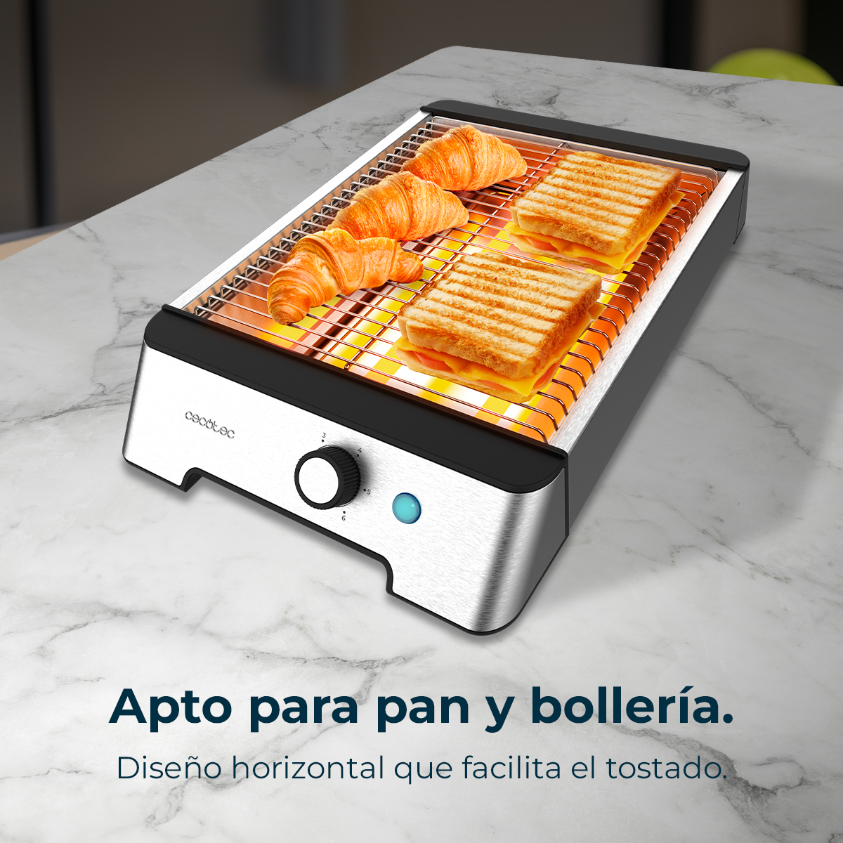 Una tostadora horizontal con cruasanes y sándwiches. Tiene un dial y una luz azul sobre una superficie de mármol.
