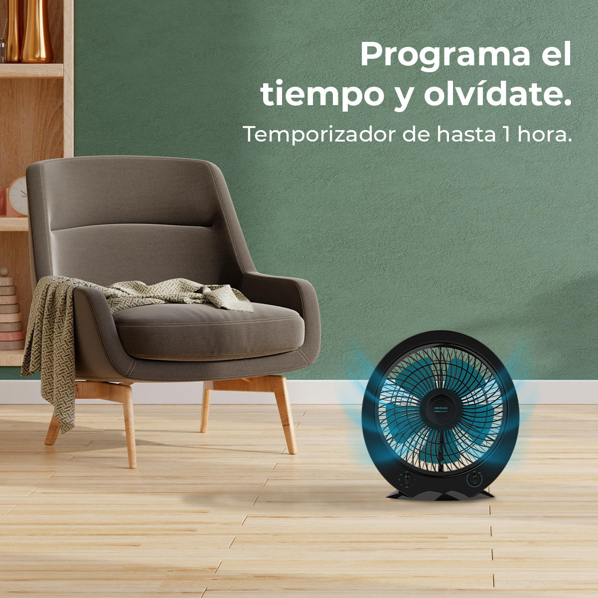 Czarny wentylator z niebieskimi łopatkami stoi na podłodze. Szary fotel z kocem w tle. Tekst na ścianie.